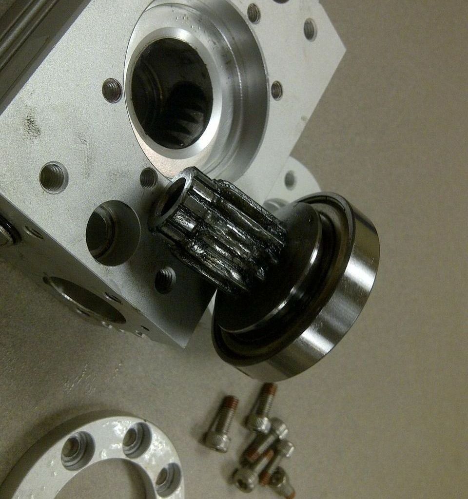 Metal machine components: shaft with splines, bearing, and block with holes, with fasteners nearby.