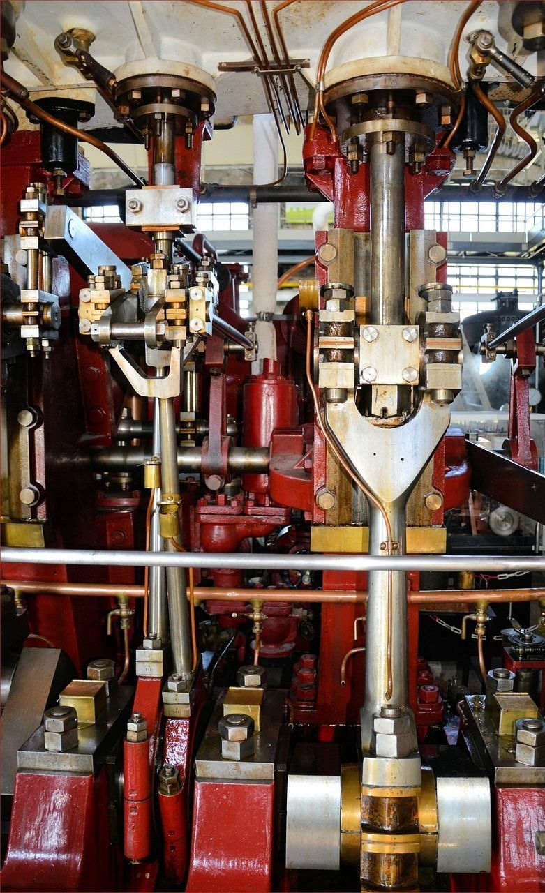 Close-up of a red and silver steam engine with pipes and mechanical parts, likely in an industrial setting.
