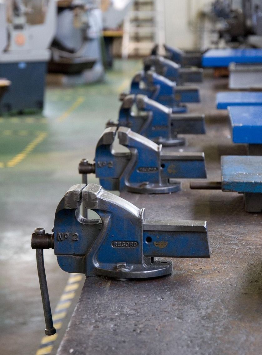 Blue vises lined up on a workbench in a workshop setting.