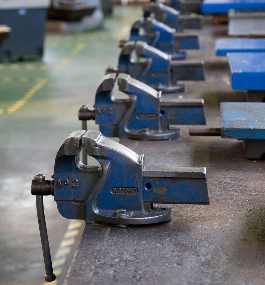 Row of blue metal vises on a workbench in a workshop.