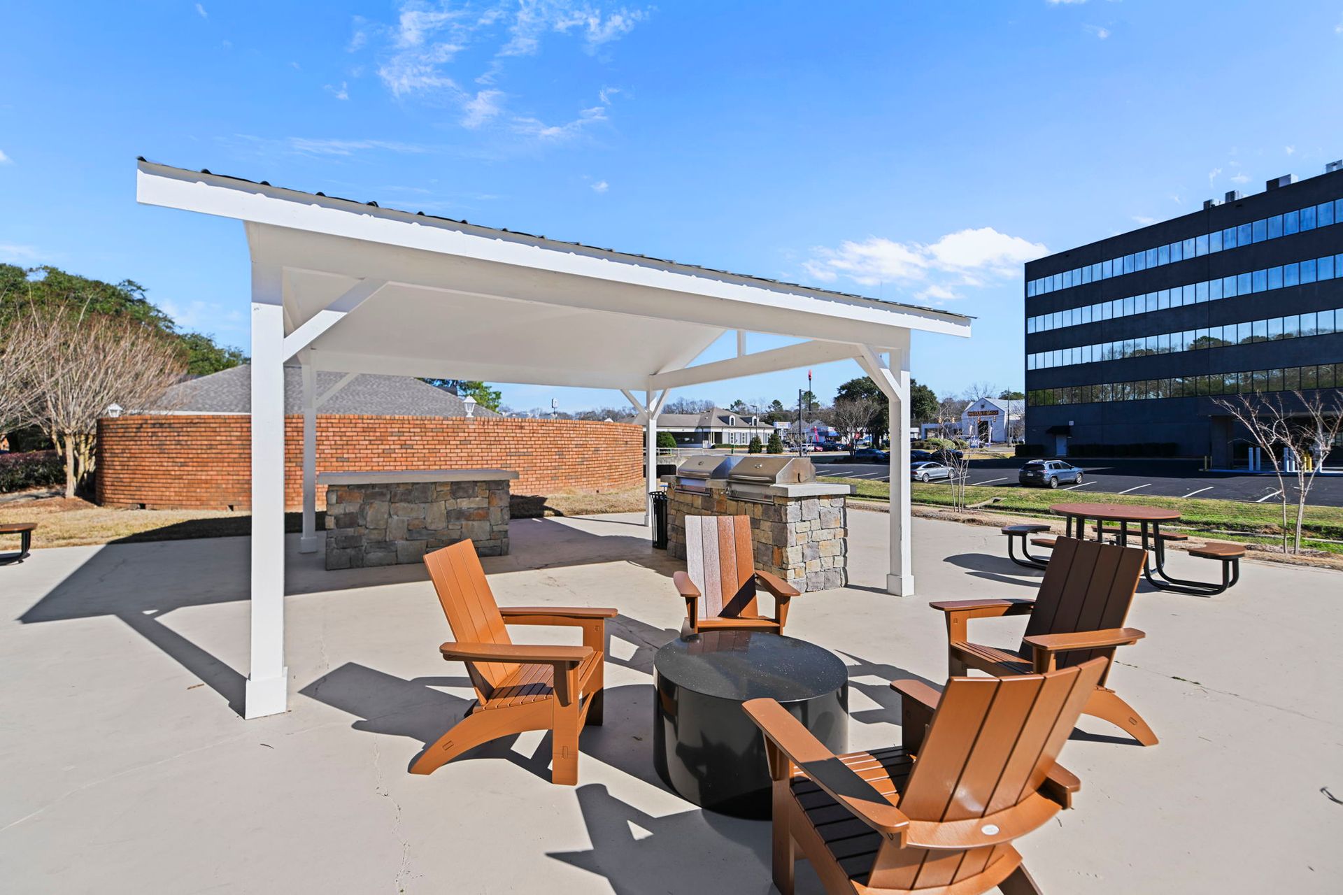 Outdoor patio featuring a white pavilion, a fire pit, several brown Adirondack chairs, and a built-in stone grill station.