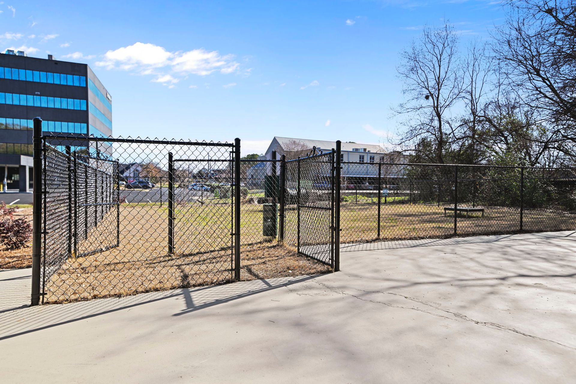 A fenced-in empty lot next to a blue office building on a sunny day.