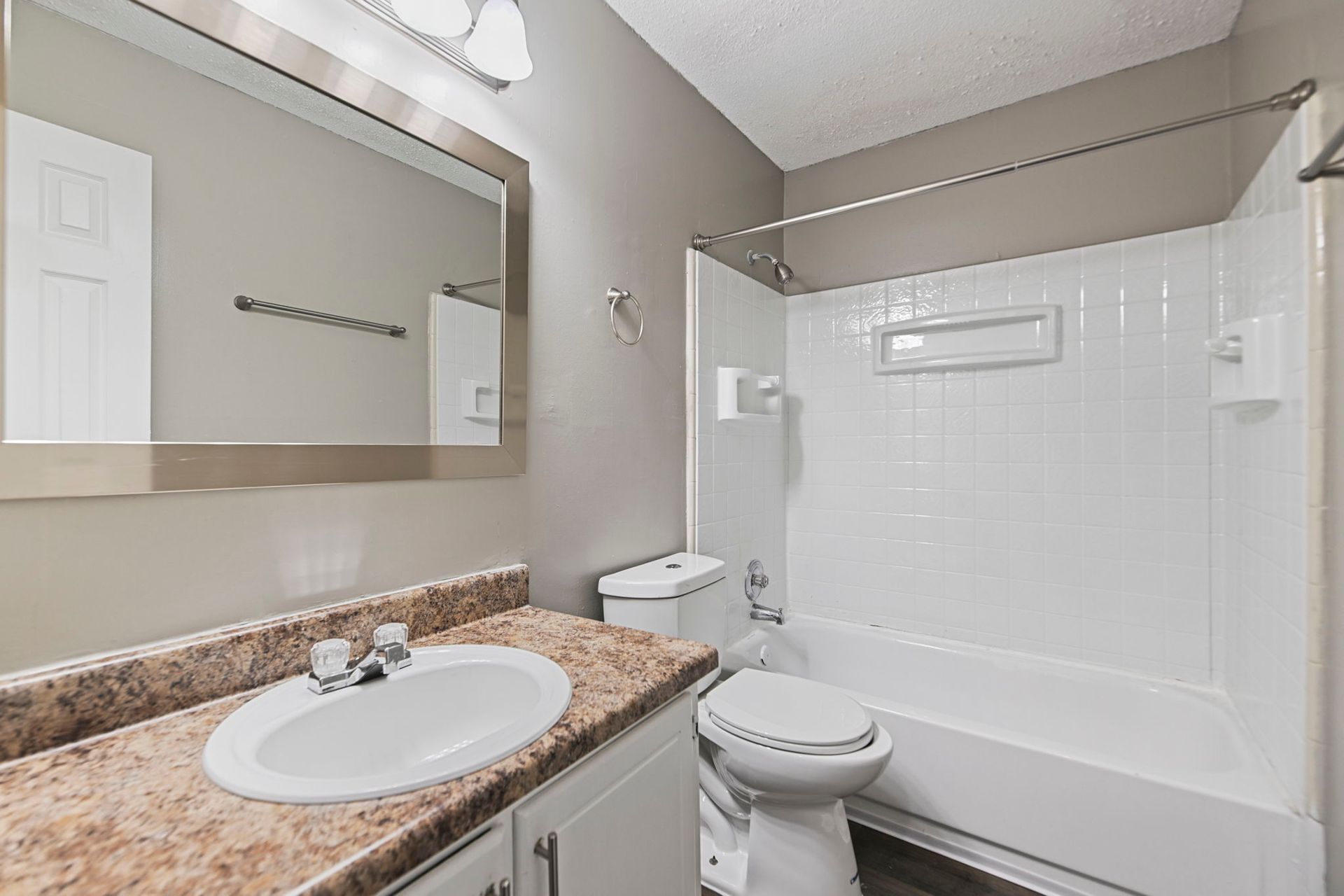 A modern bathroom featuring a beige countertop vanity, a white oval sink, a wall mirror, and a white tiled shower-tub combo.