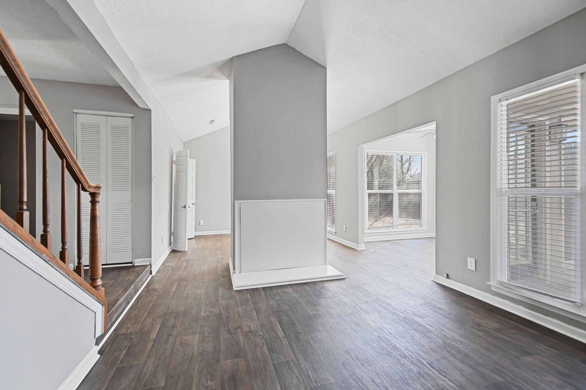 Interior view of an empty living area with grey walls, dark wood floors, a central fireplace, and a wooden staircase.