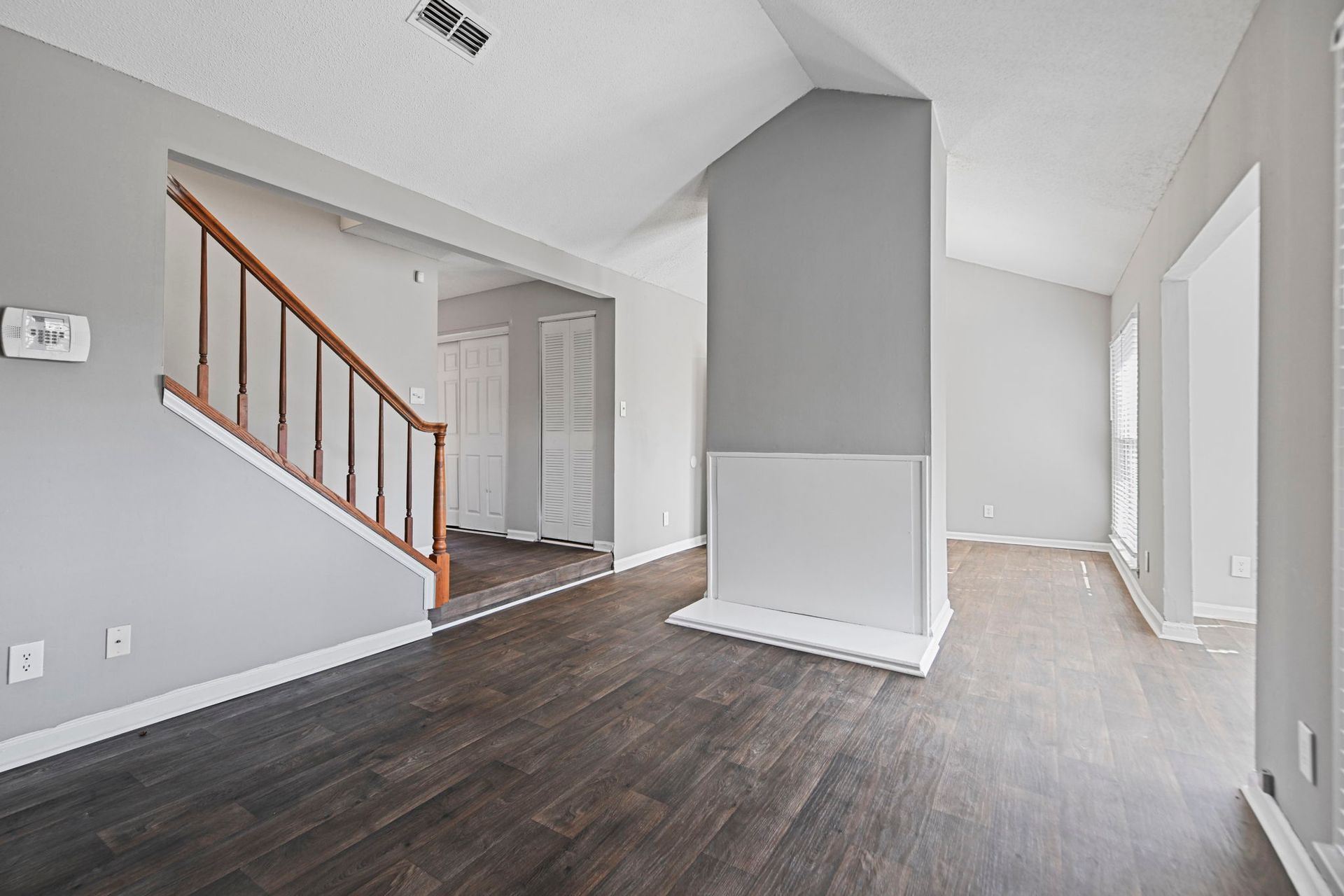 A bright, empty living room with wood-look floors, a central fireplace, and a staircase leading to an upper level.