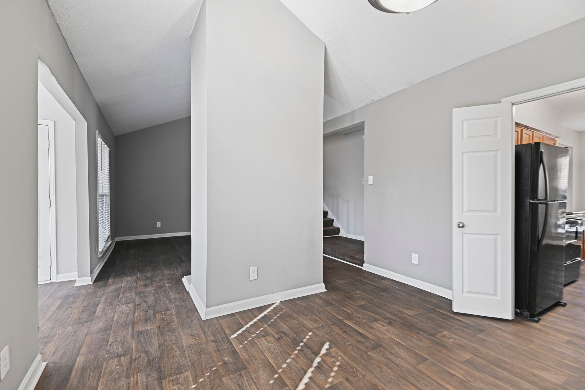 An interior view of a room with light grey walls, wood-look flooring, a large central pillar, and a black refrigerator.