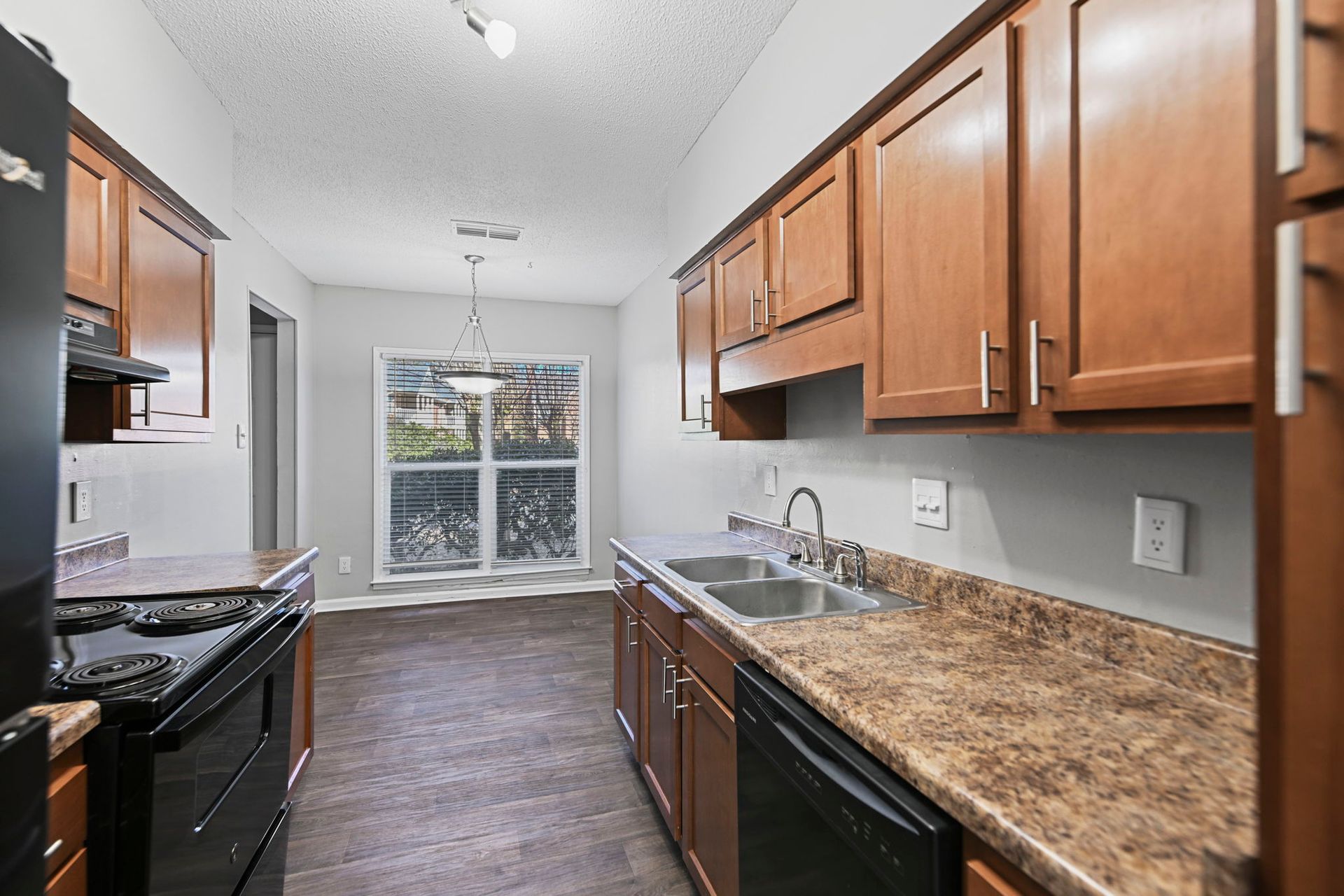 A galley kitchen with brown wooden cabinets, a black stove and dishwasher, and a window in the background.