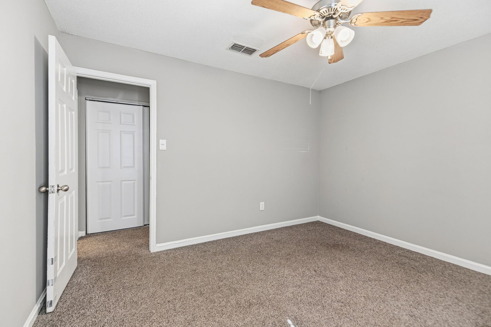An empty bedroom with gray walls, beige carpeting, a white door, and a ceiling fan.