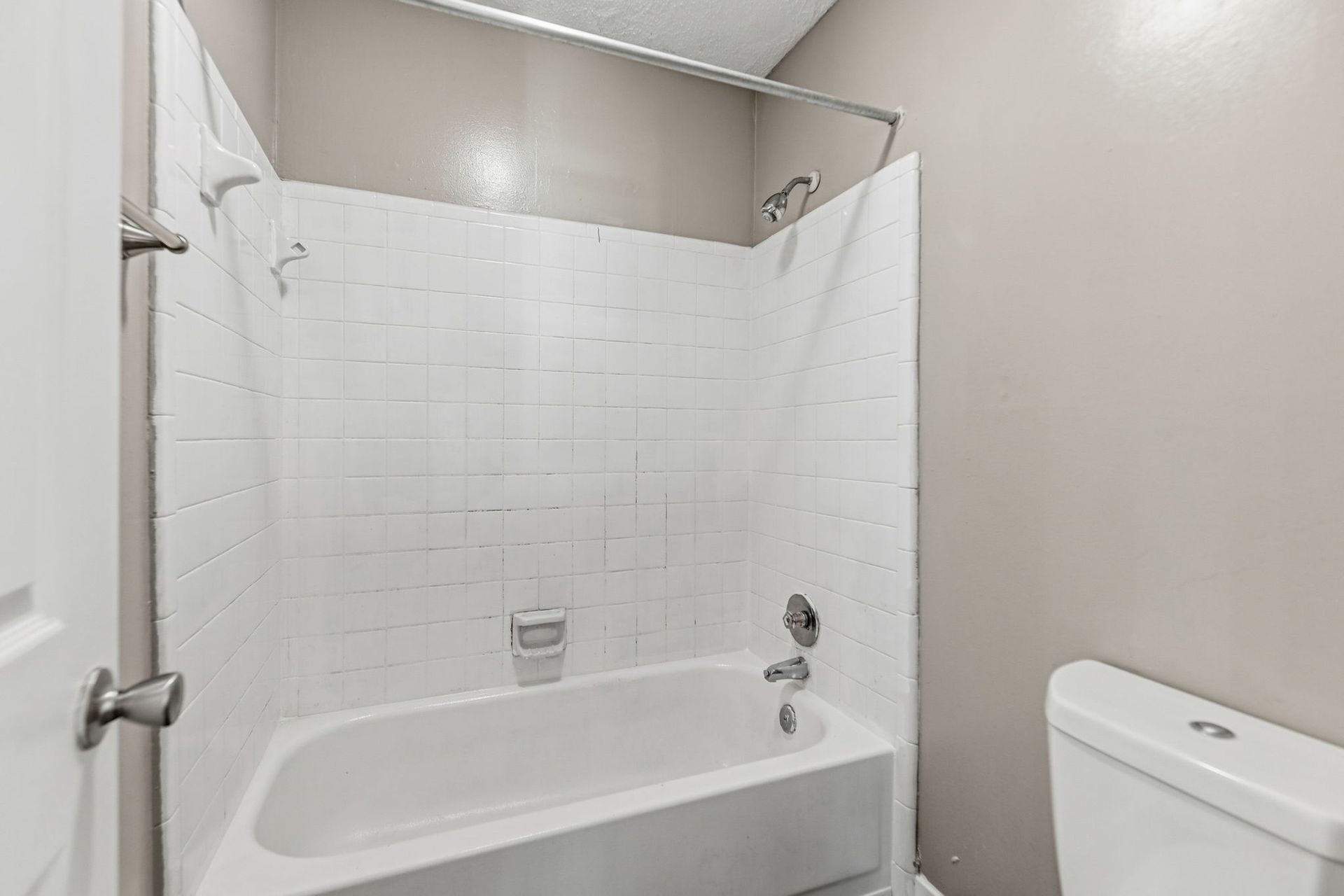 A bathroom featuring a white bathtub with a tiled shower surround, a chrome shower head, and a white toilet.