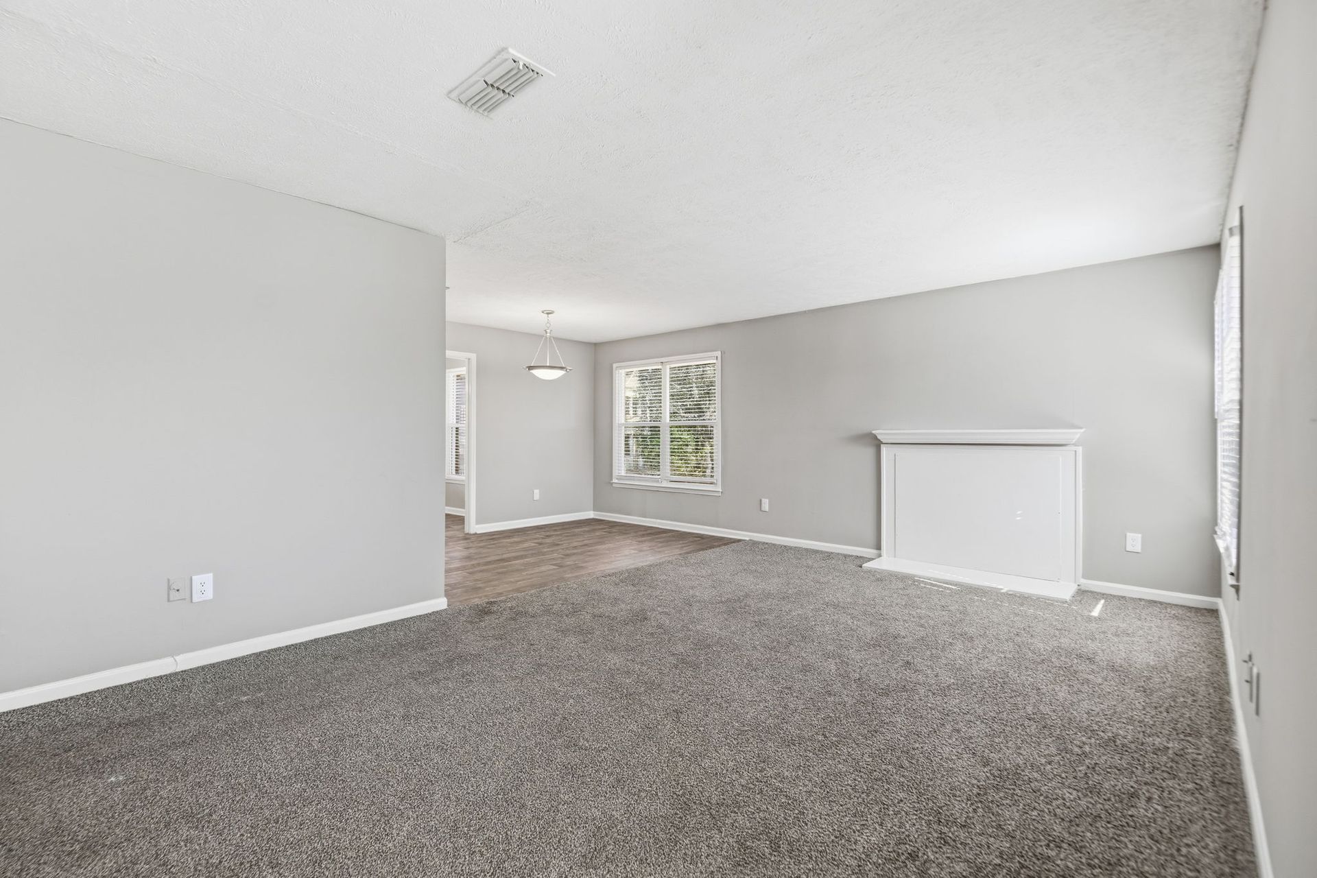 Empty carpeted living room with grey walls, a white fireplace, and a doorway leading to a dining area.