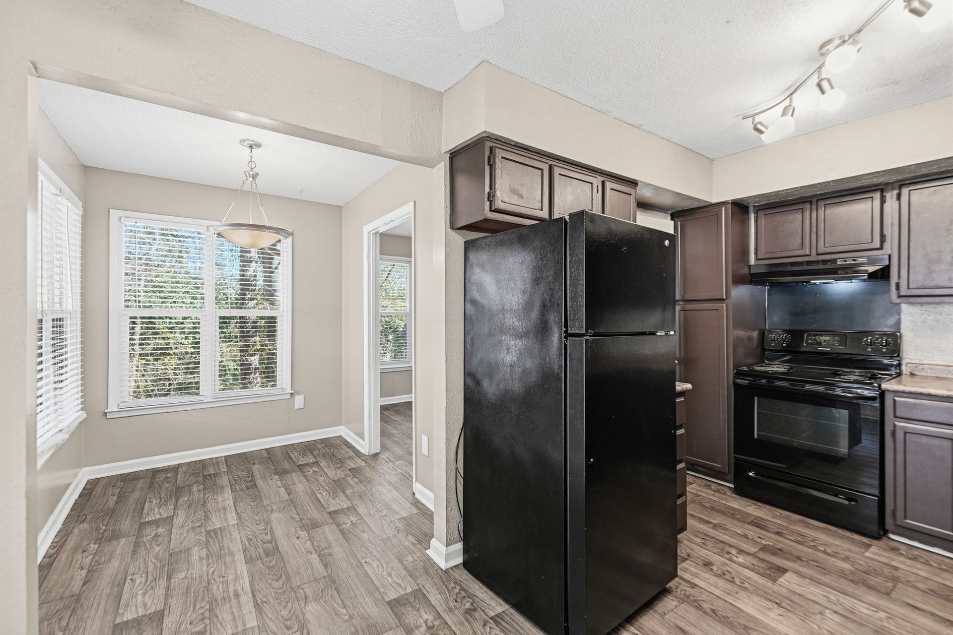 A kitchen and adjacent dining area featuring wood-look floors, brown cabinetry, and black appliances.