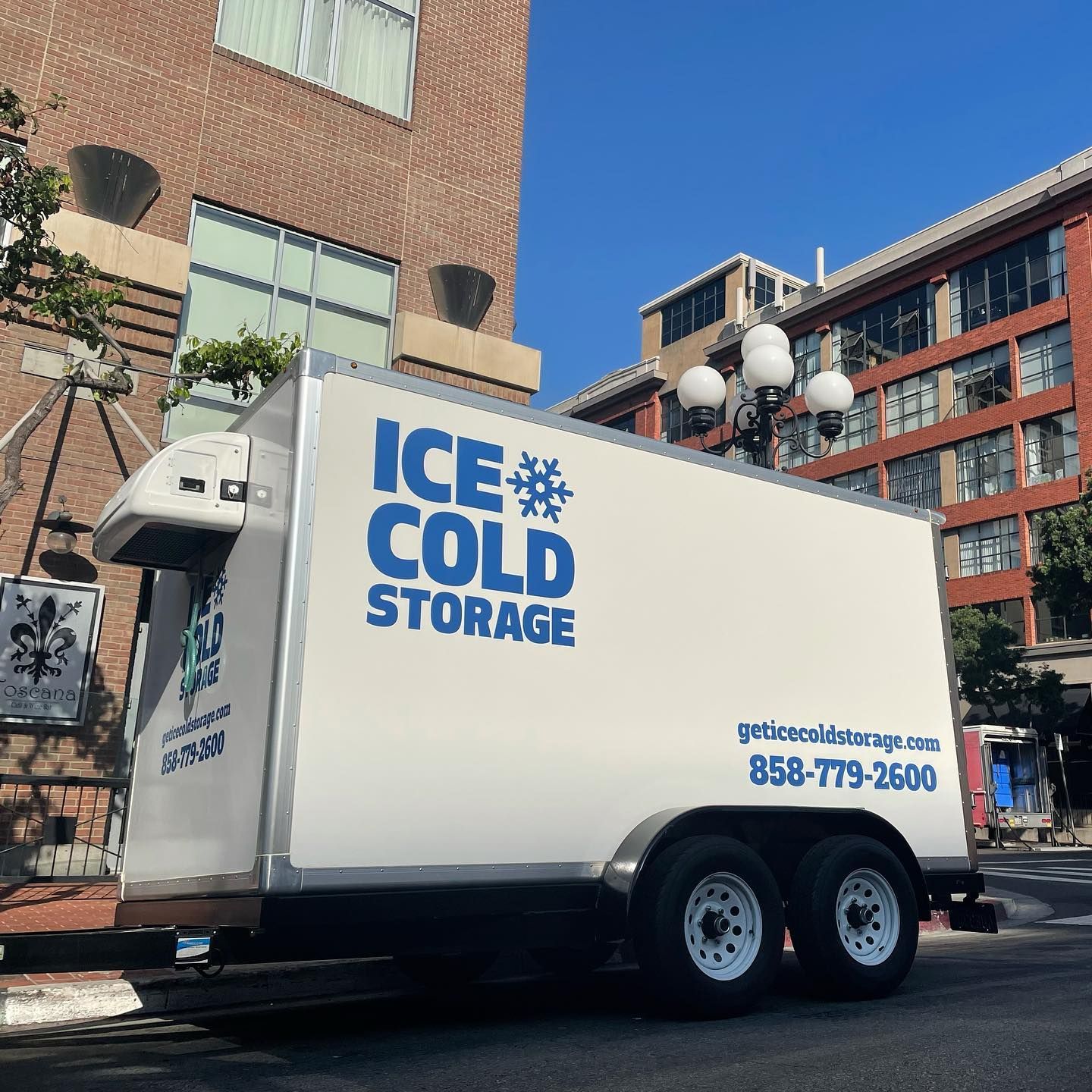 An ice cold storage truck is parked in front of a building
