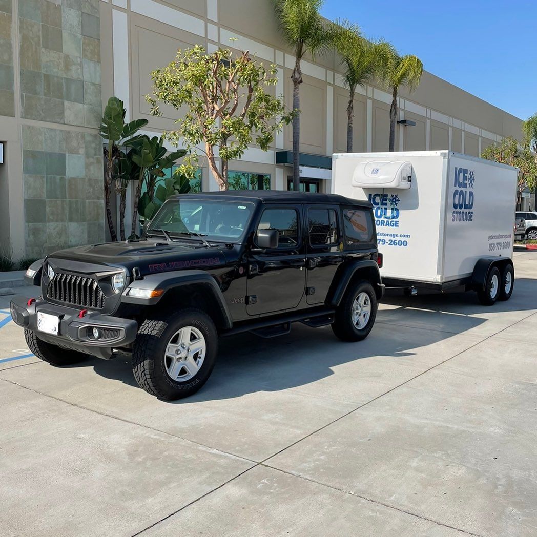 A black jeep is parked next to a white trailer that says ice cold