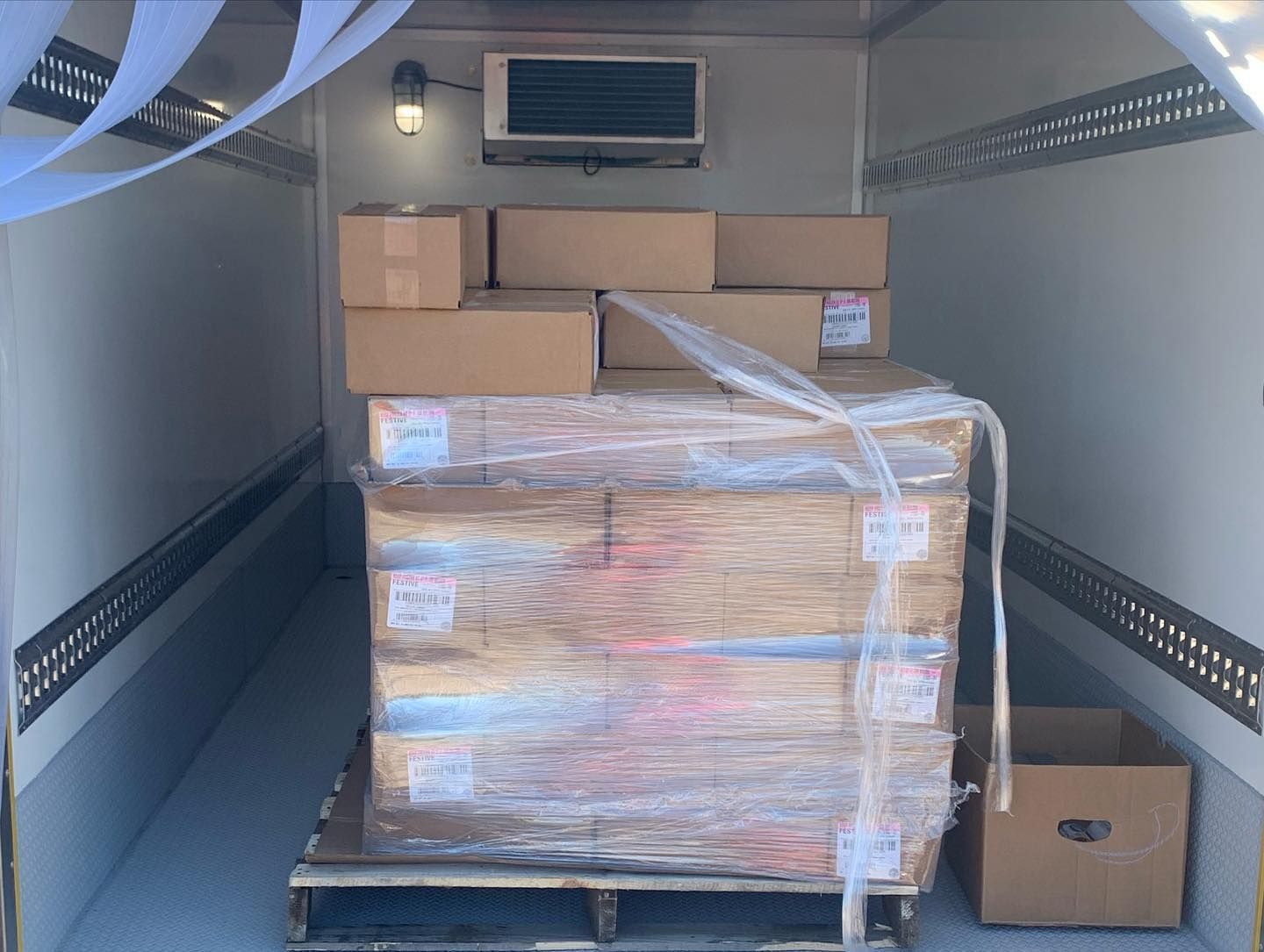 A large stack of cardboard boxes wrapped in plastic is in the back of a truck.