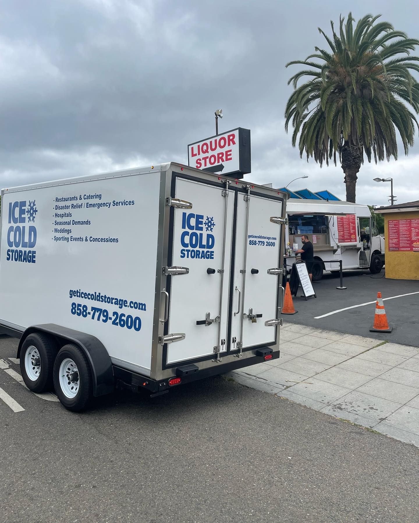 A trailer for ice cold storage is parked in front of a liquor store.