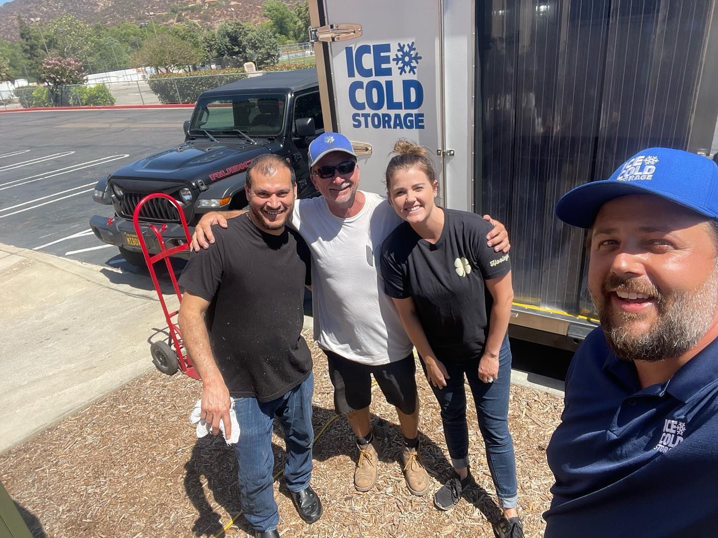 A group of people are posing for a picture in front of an ice cold storage truck.