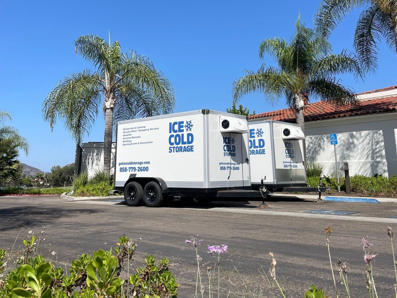 Two ice cold storage trailers are parked in a parking lot.