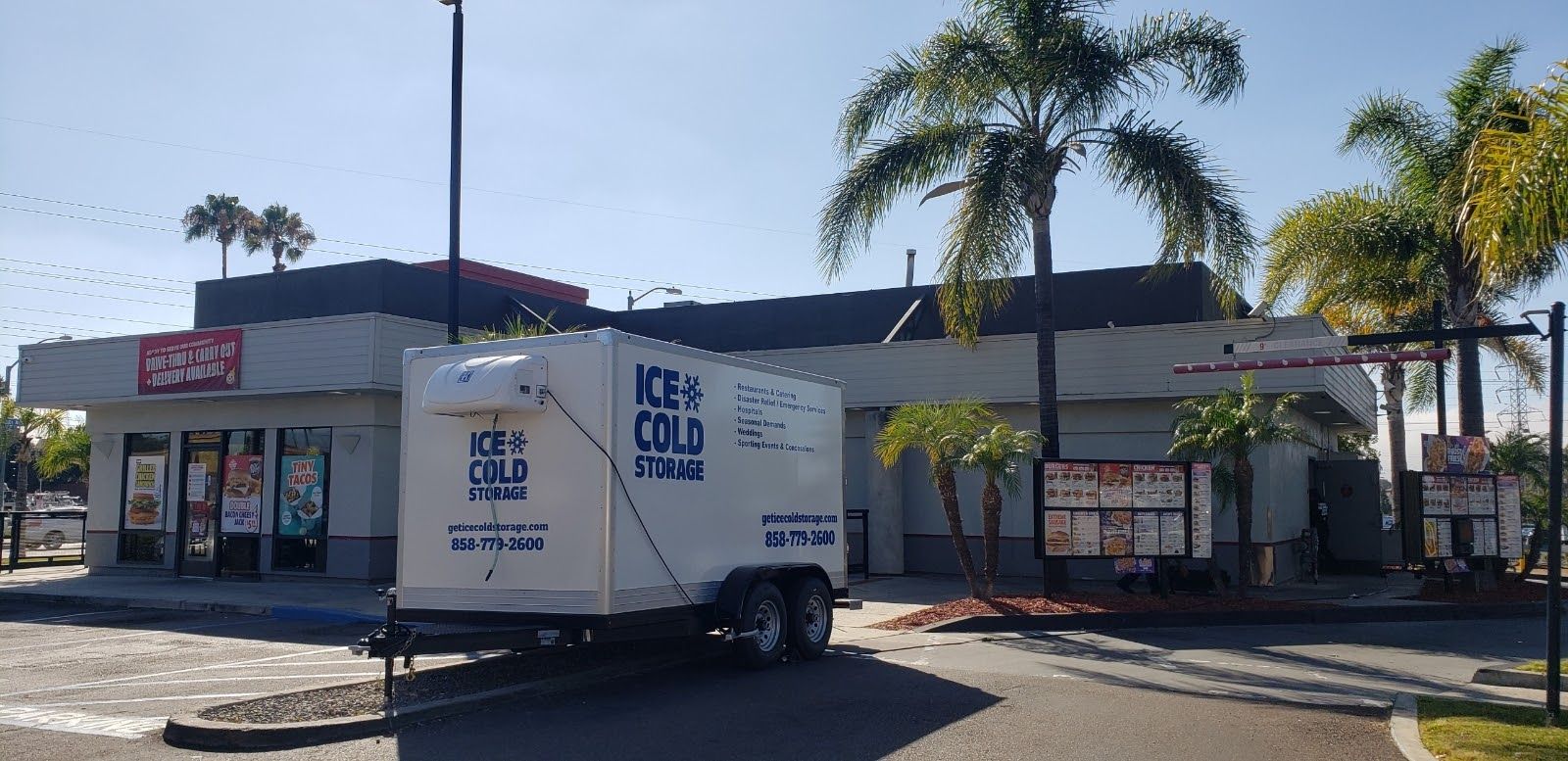 A white trailer is parked in front of a fast food restaurant.