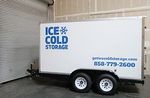 A white trailer with the words `` ice cold storage '' written on it is parked in a garage.