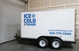 A white trailer with the words `` ice cold storage '' written on it is parked in a garage.