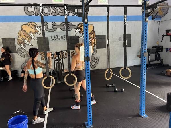 Two people in a CrossFit gym in Bunnell, FL with rings hanging from a pull-up rig and painted wall mural in the background.