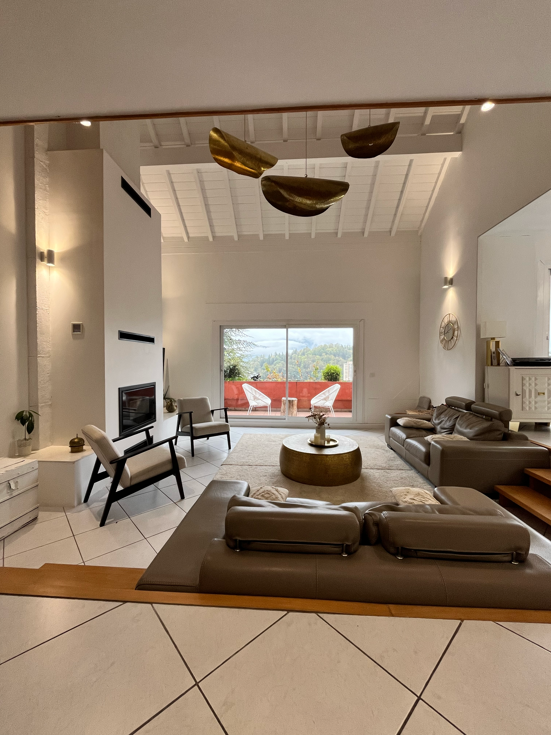 Spacieux salon blanc avec cheminée, mobilier moderne et vue depuis un balcon.