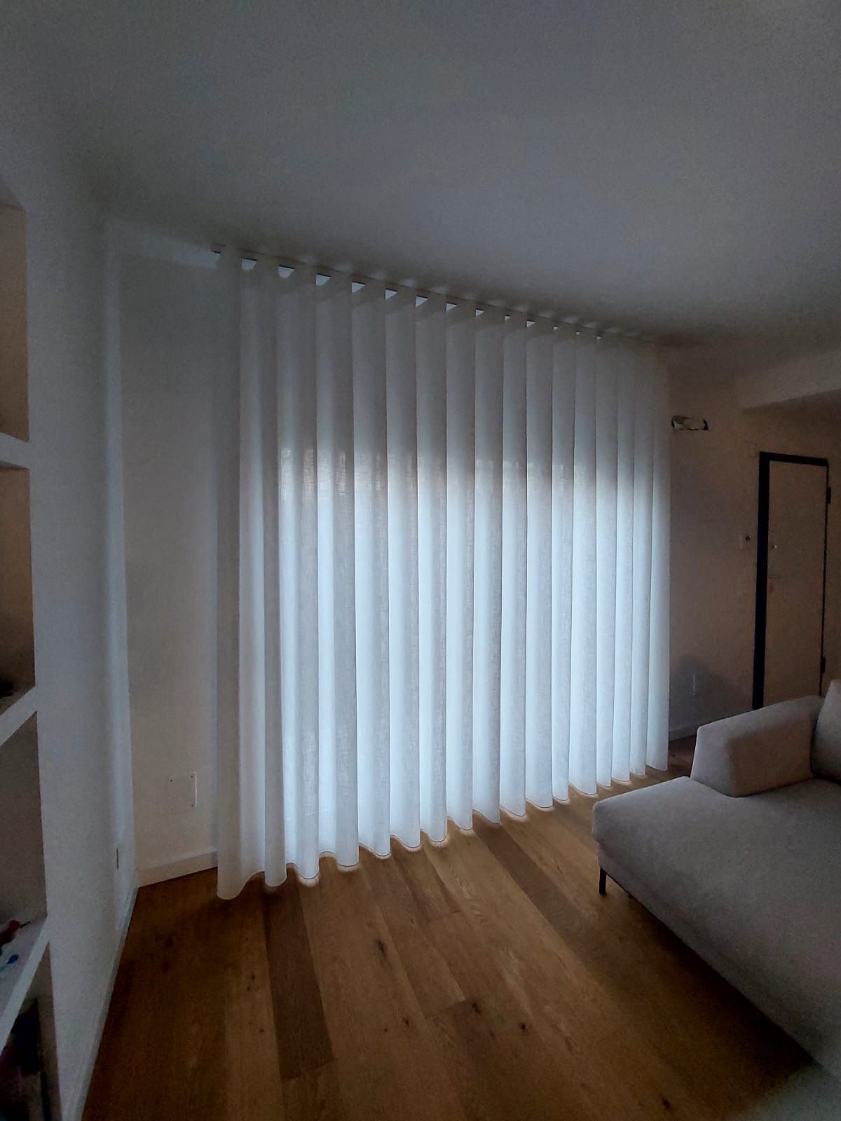 Un soggiorno con un divano e una finestra con tende bianche.