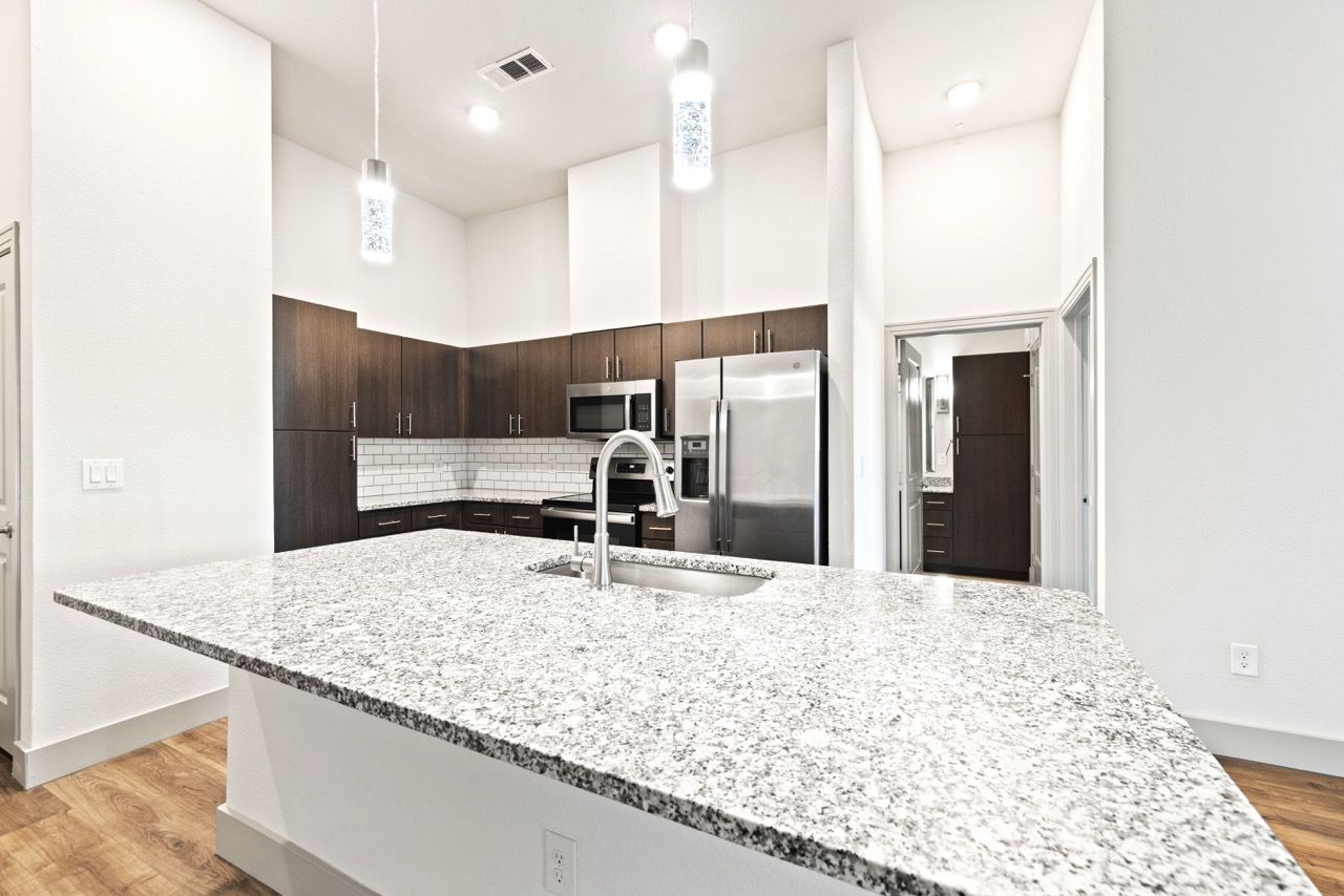 Modern apartment kitchen with granite island, stainless steel appliances, and pendant lights at Olympus Hudson Oaks.