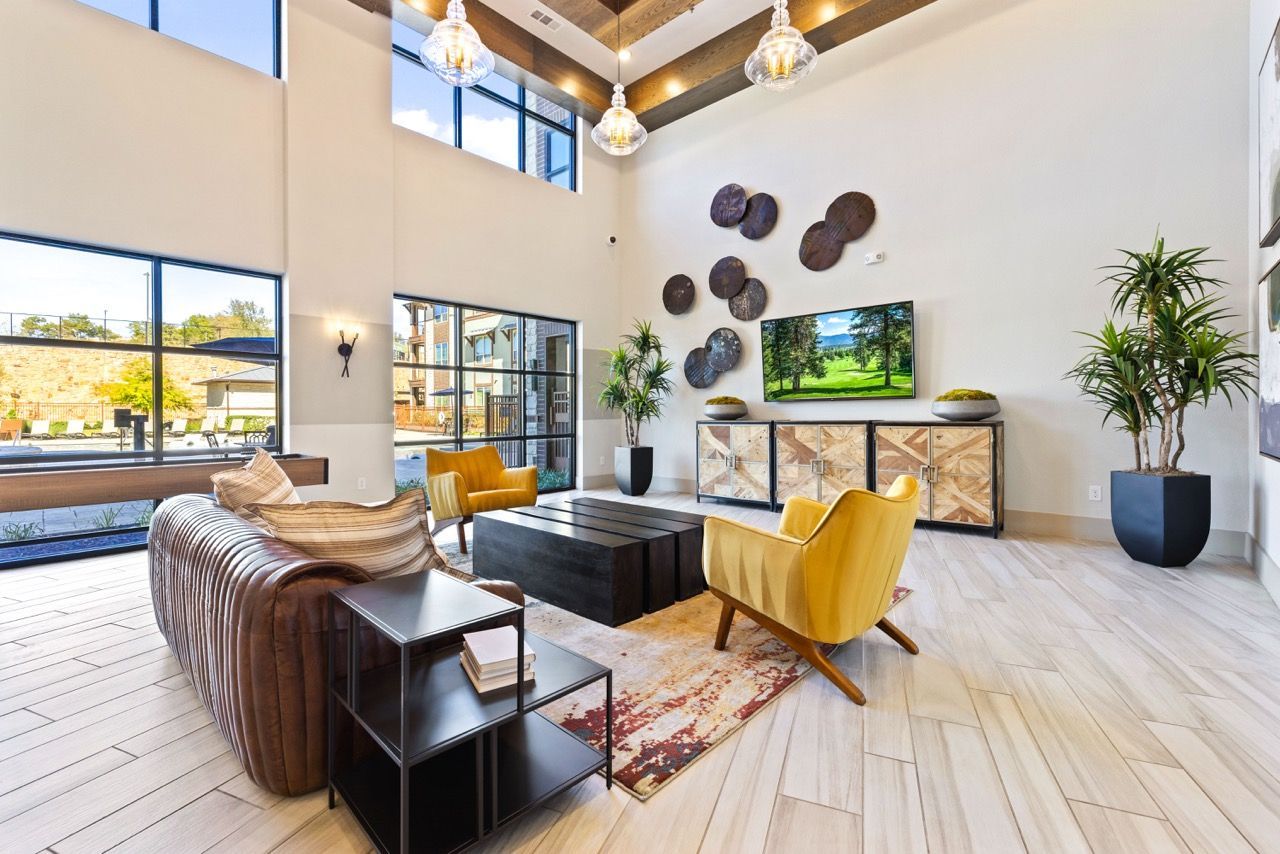 Bright, modern community lounge with yellow armchairs, sofa, TV, and large windows at Olympus Hudson Oaks.