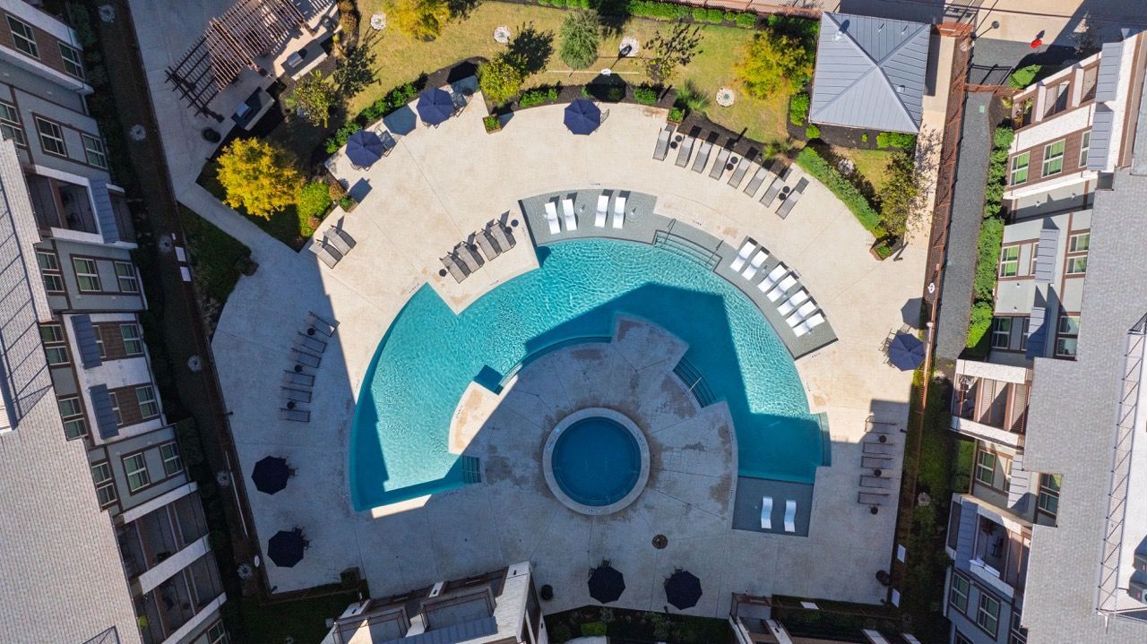 Aerial view of a curved swimming pool in a courtyard surrounded by apartment buildings at Olympus Hudson Oaks.