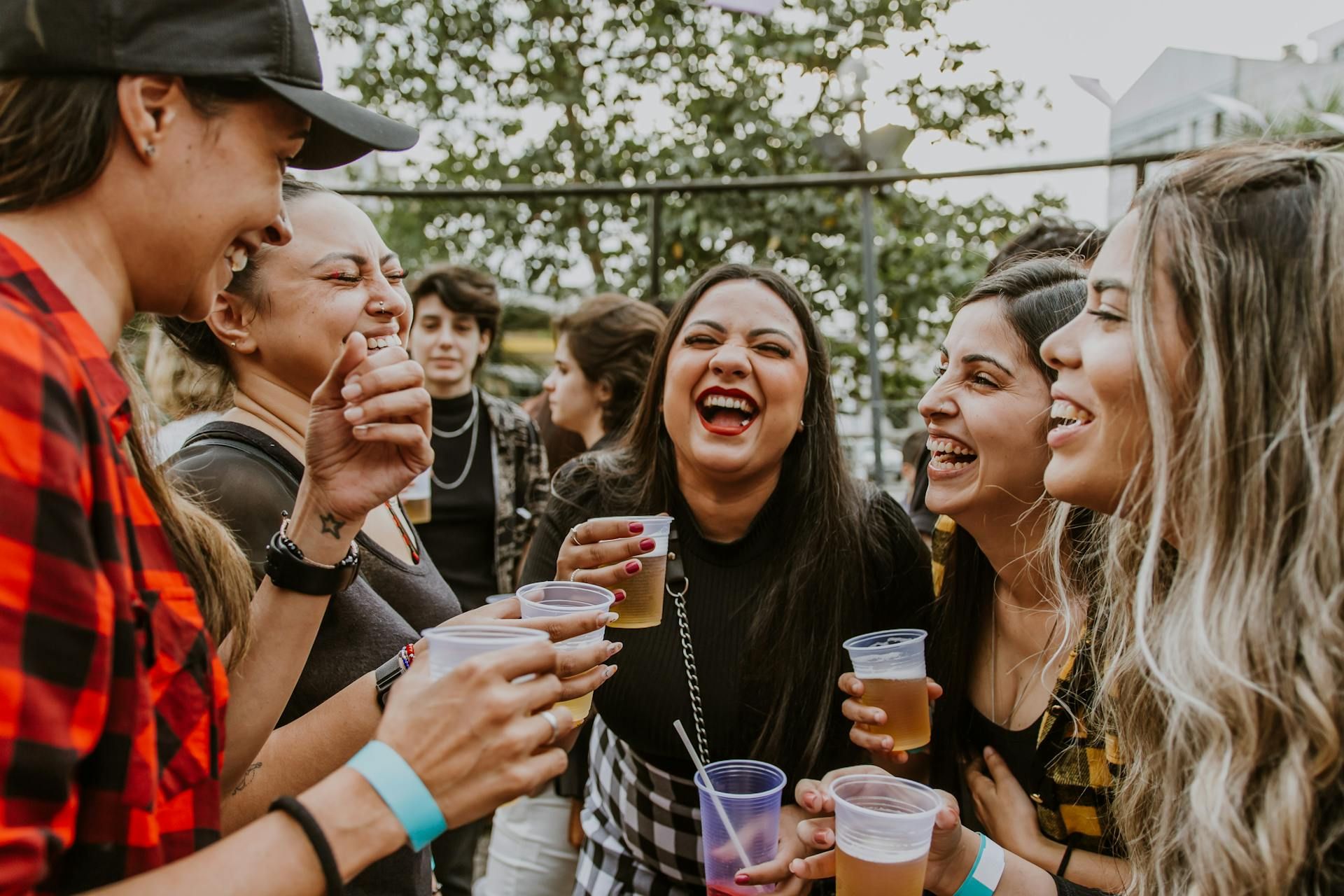A group of friends laughing and holding plastic cups at an outdoor gathering.