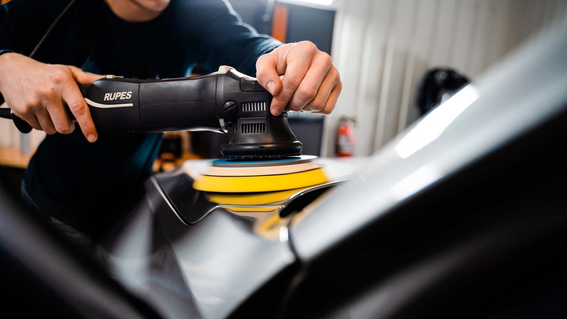 A person wearing black gloves is cleaning a car with a brush.