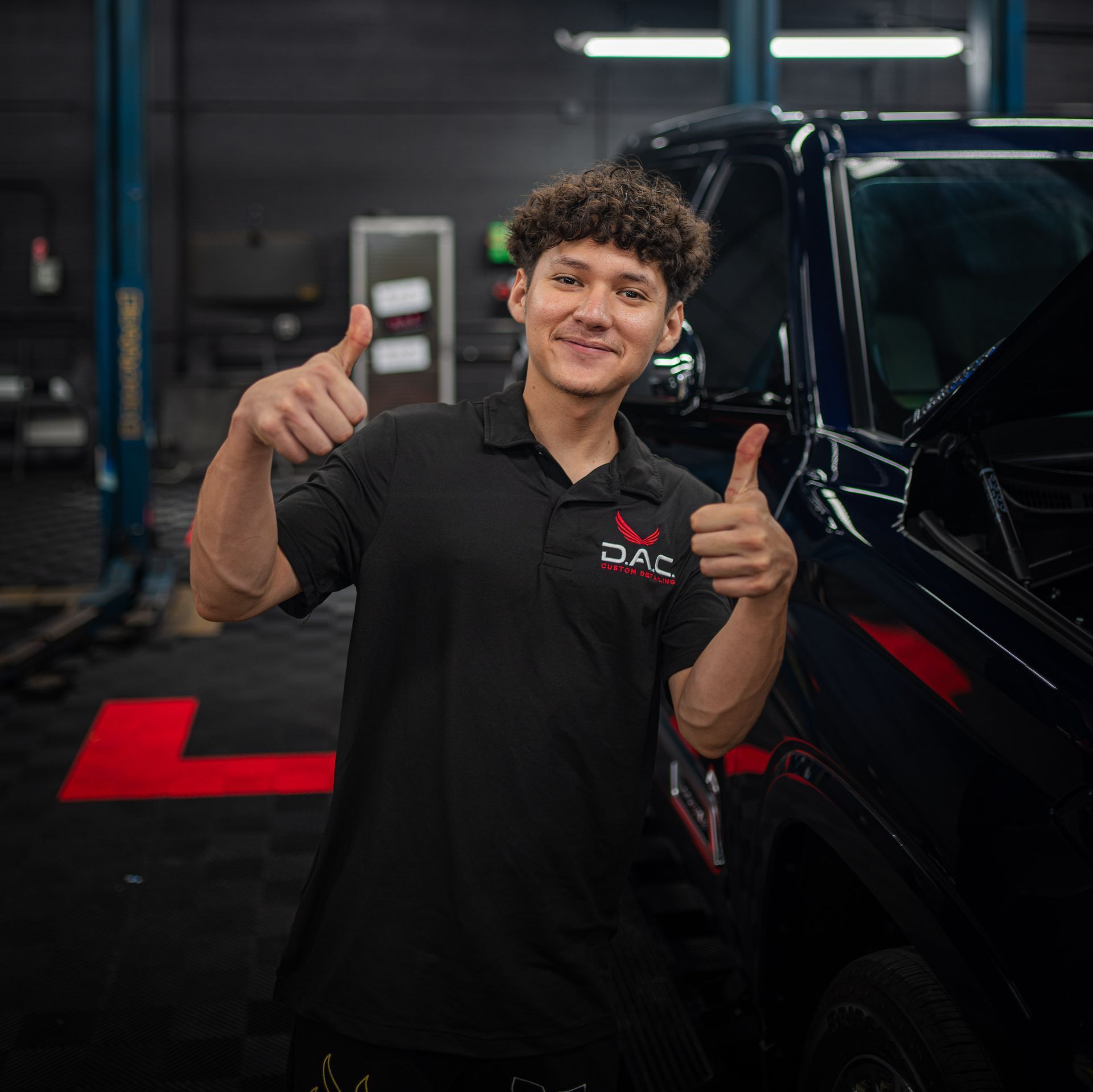 A man in a black shirt is giving a thumbs up in front of a truck.