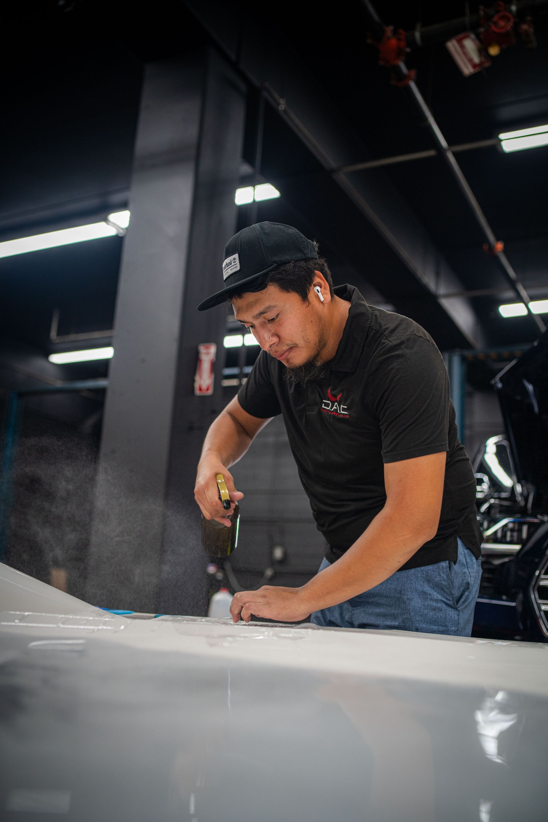 A man in a red shirt is working on the hood of a car.