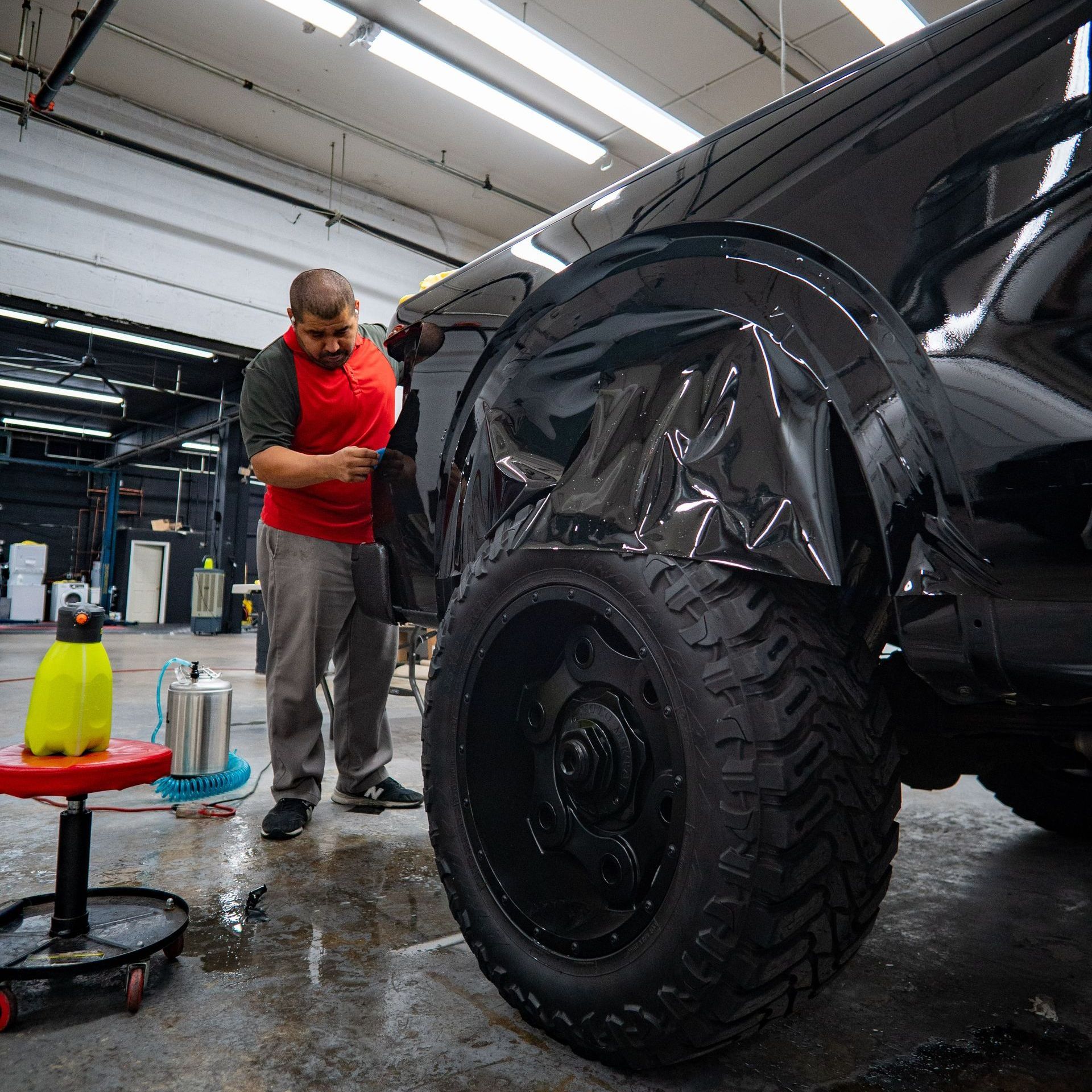 A man is standing next to a black truck in a garage.