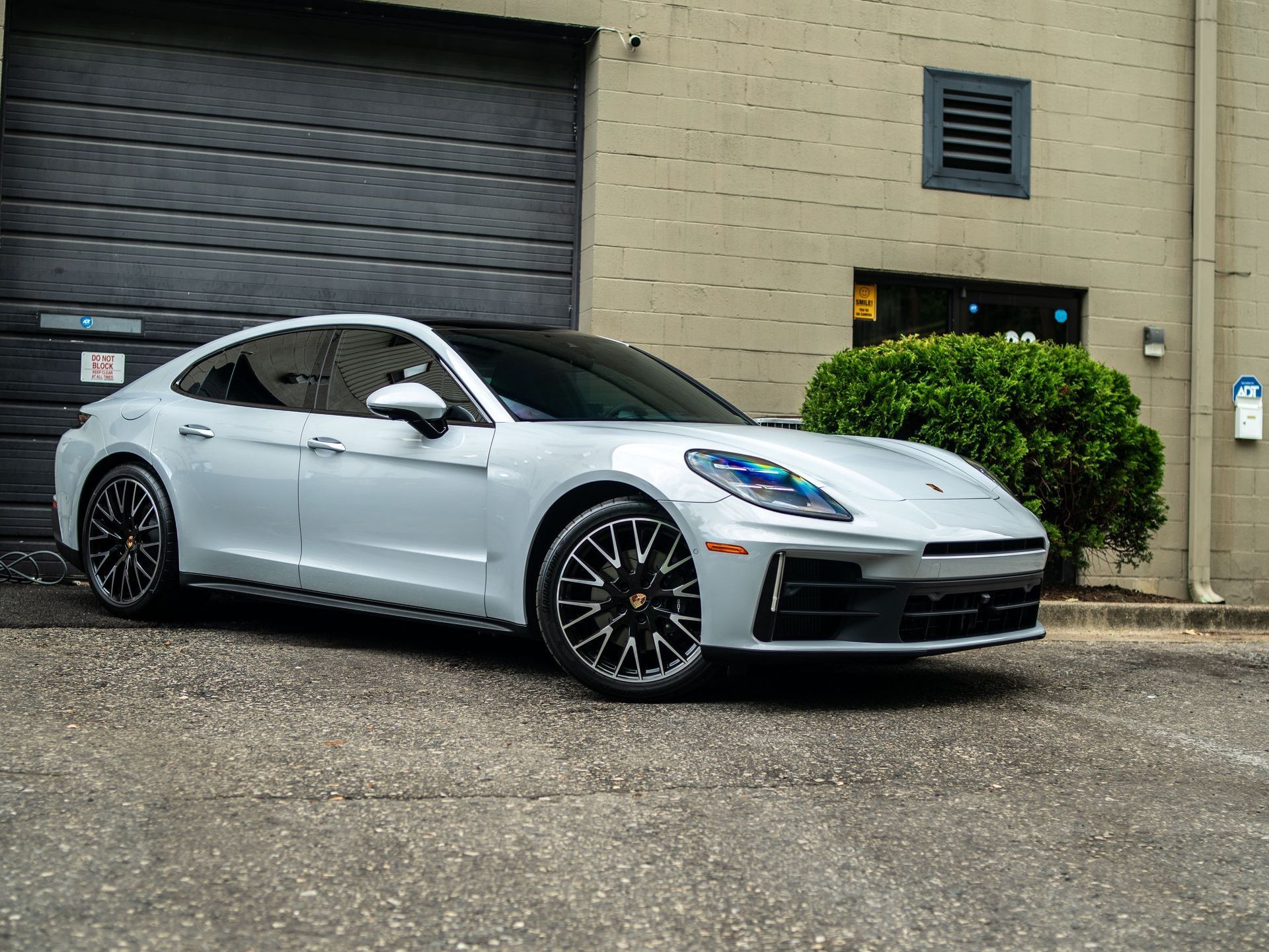 A white porsche panamera is parked in front of a building.