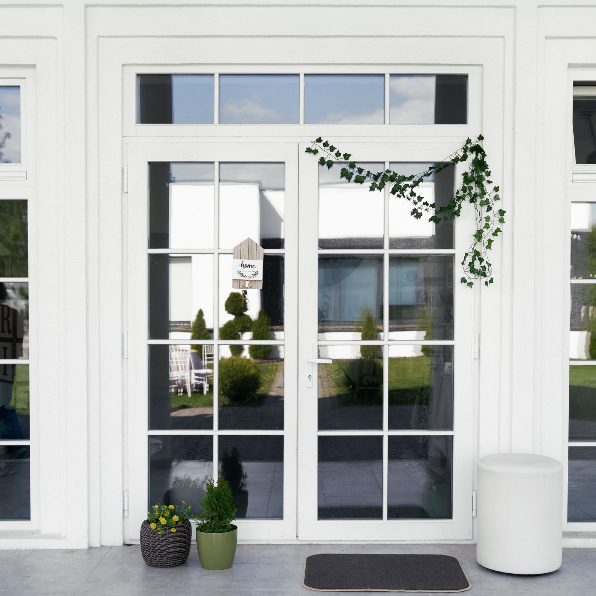 White double doors with glass panels; vine, potted plants, and a stool decorate the entrance.