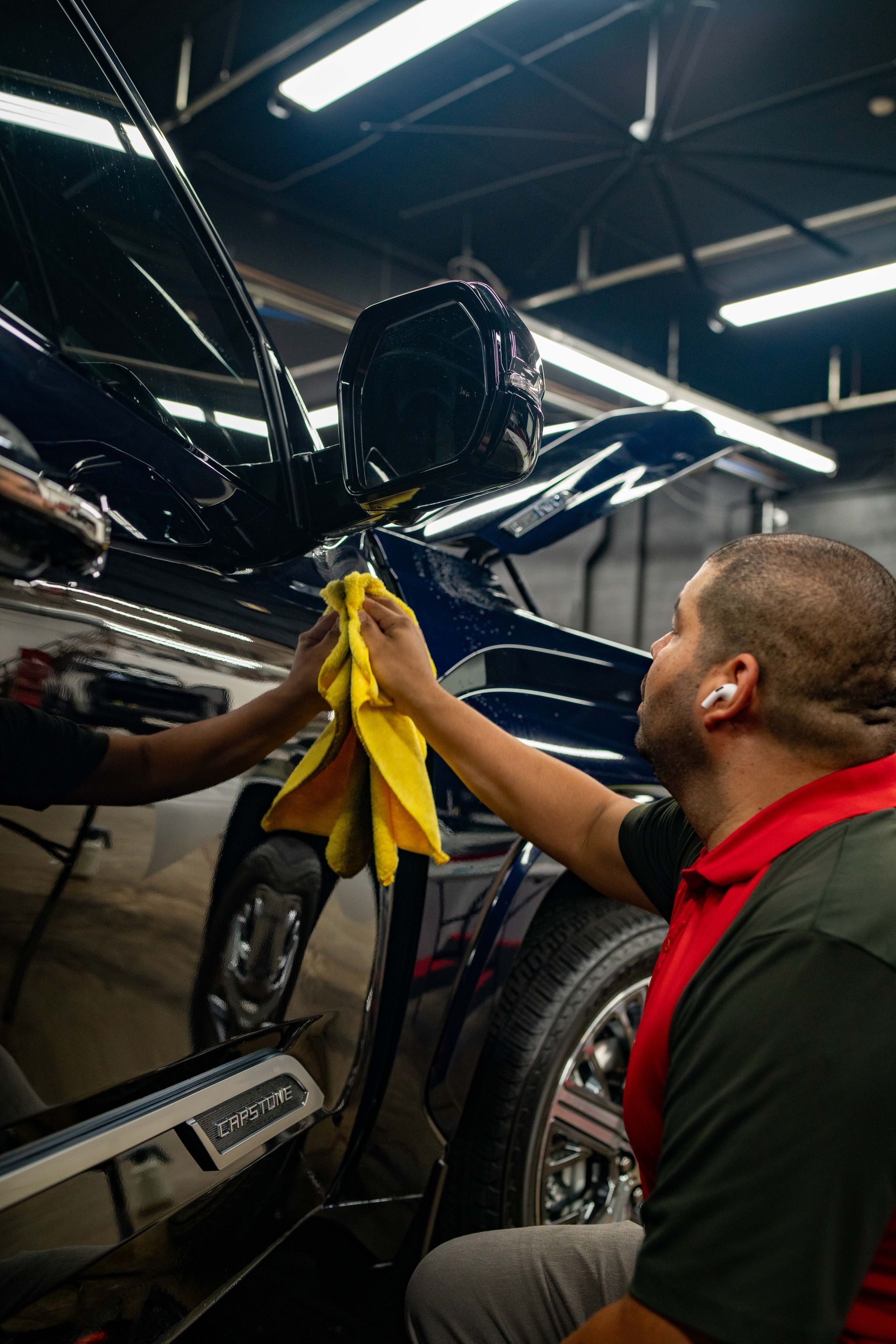 A man in a red shirt is working on the hood of a car.