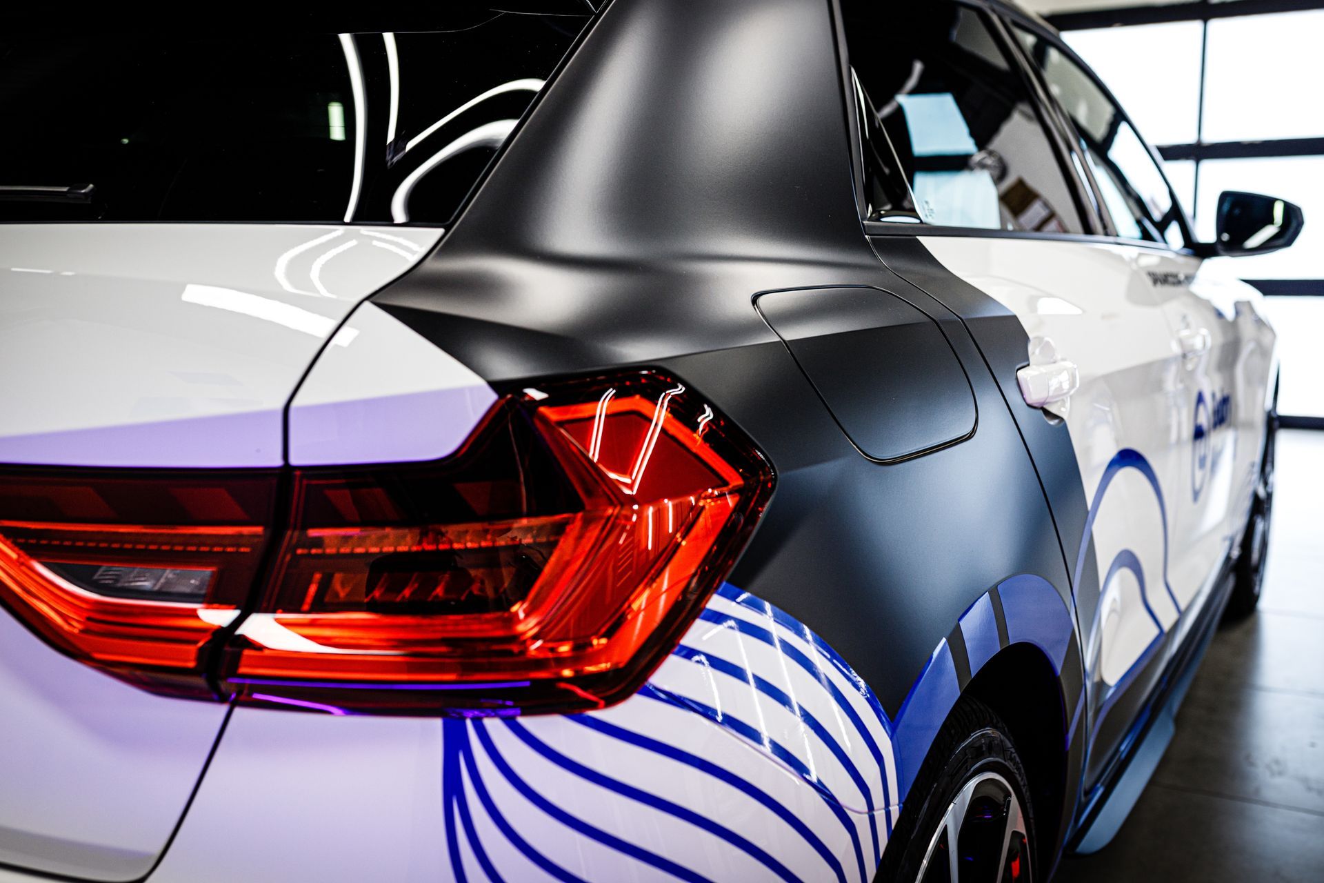 White and black car with a graphic wrap, showcasing the rear with a taillight and a garage background.