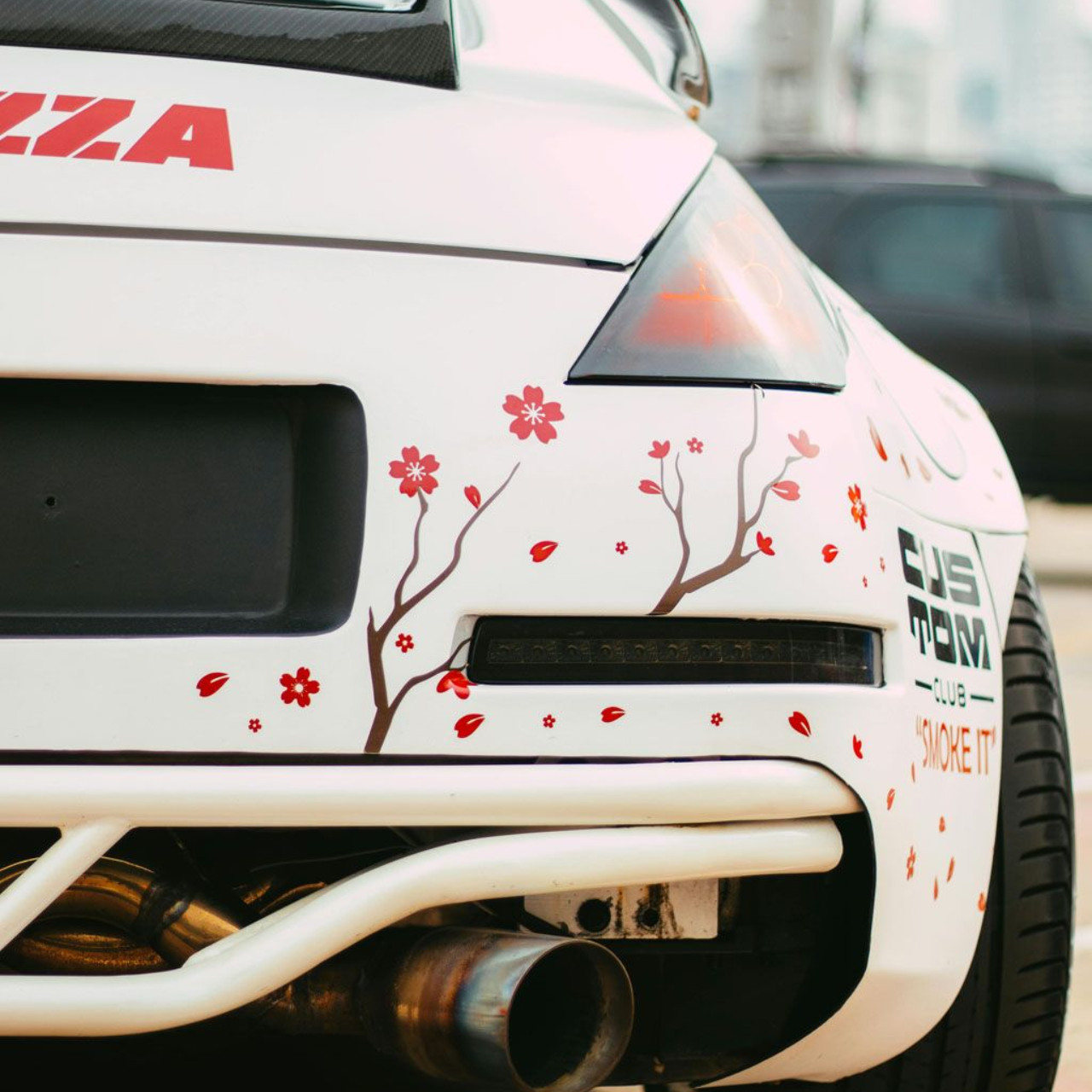 White sports car rear with cherry blossom decal, large exhaust pipe.
