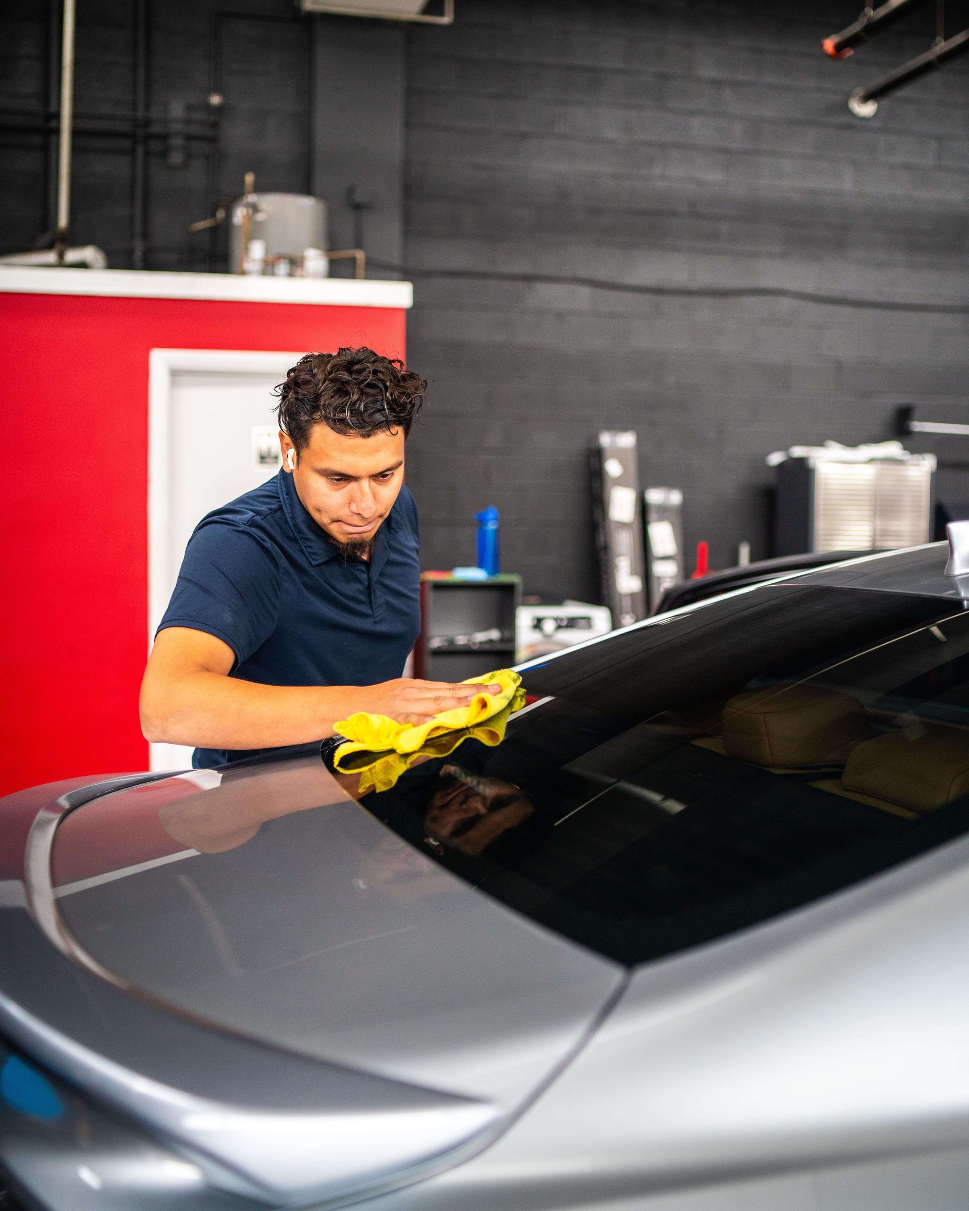 A man is cleaning the windshield of a car in a garage.