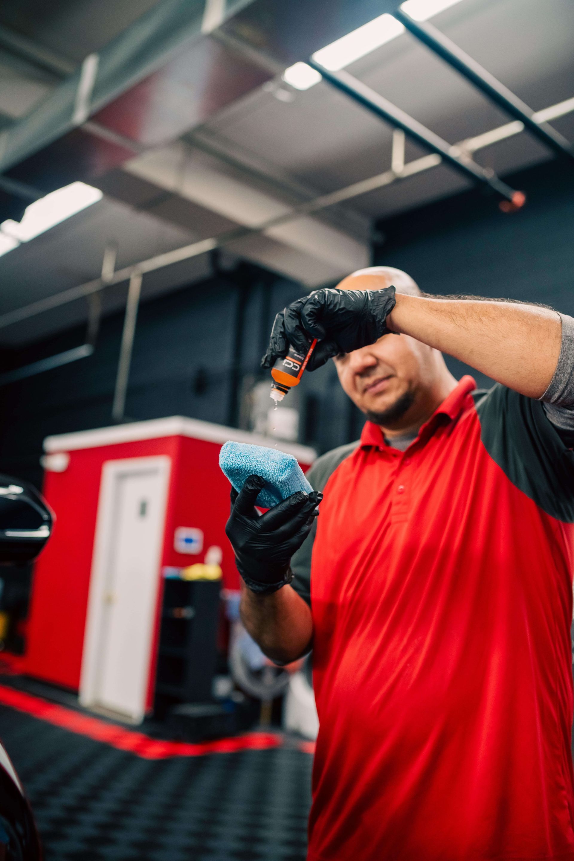 A person wearing black gloves is polishing a red car.