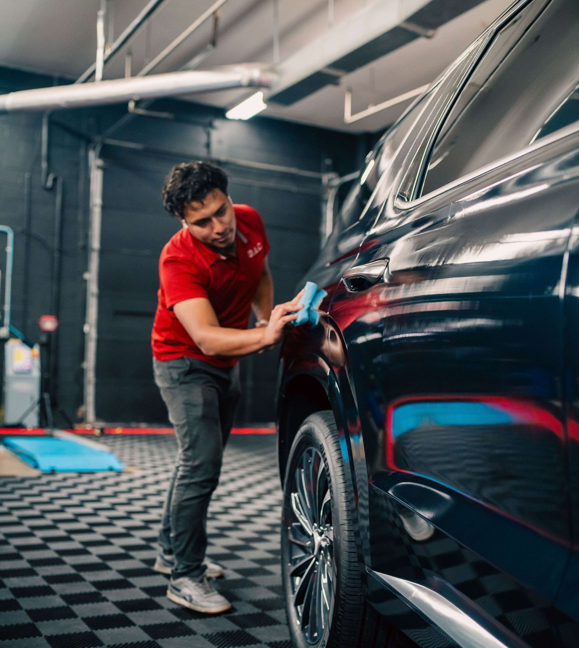 A man in a red shirt is working on the hood of a car.