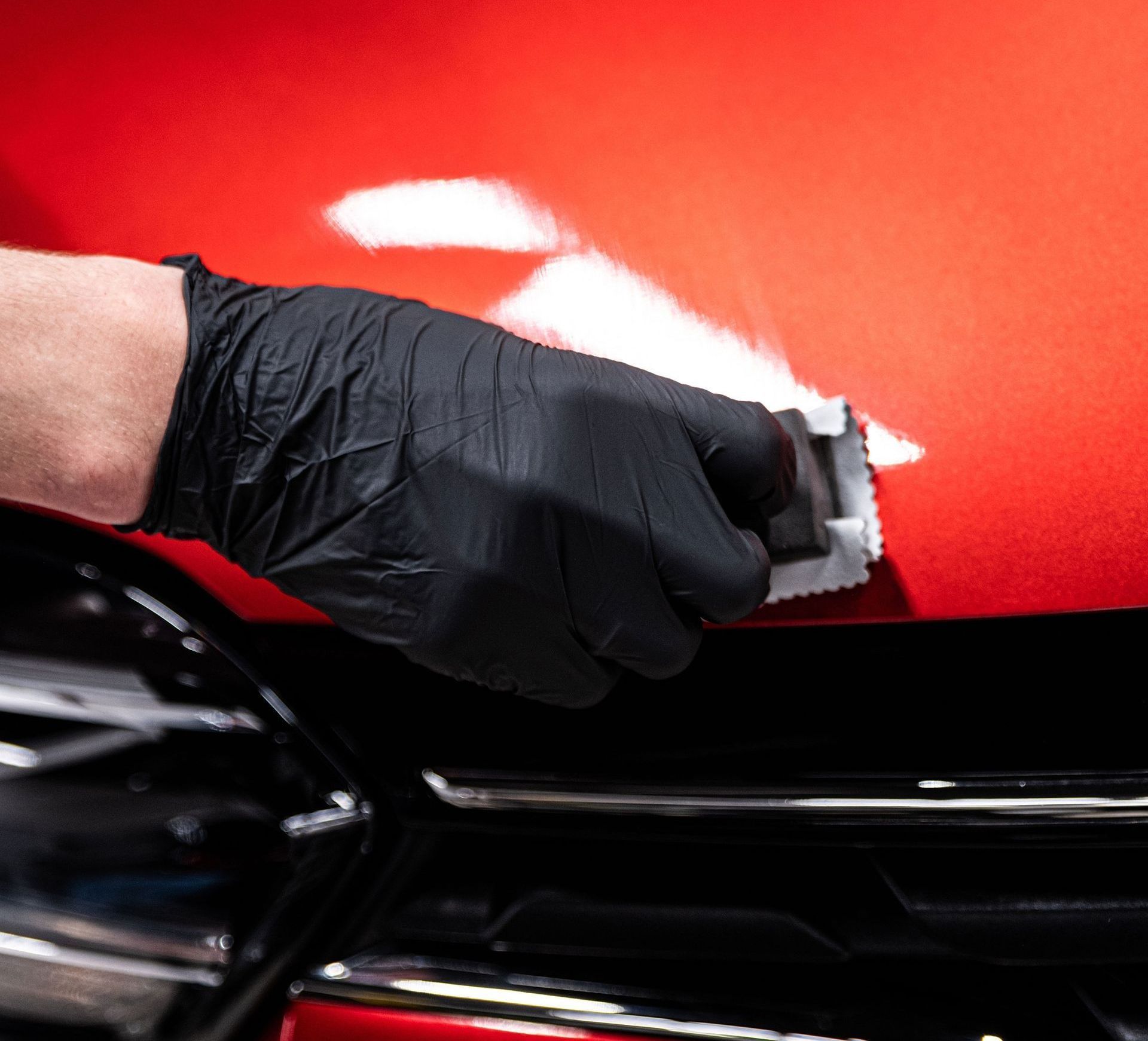 A man in a red shirt is working on the hood of a car.