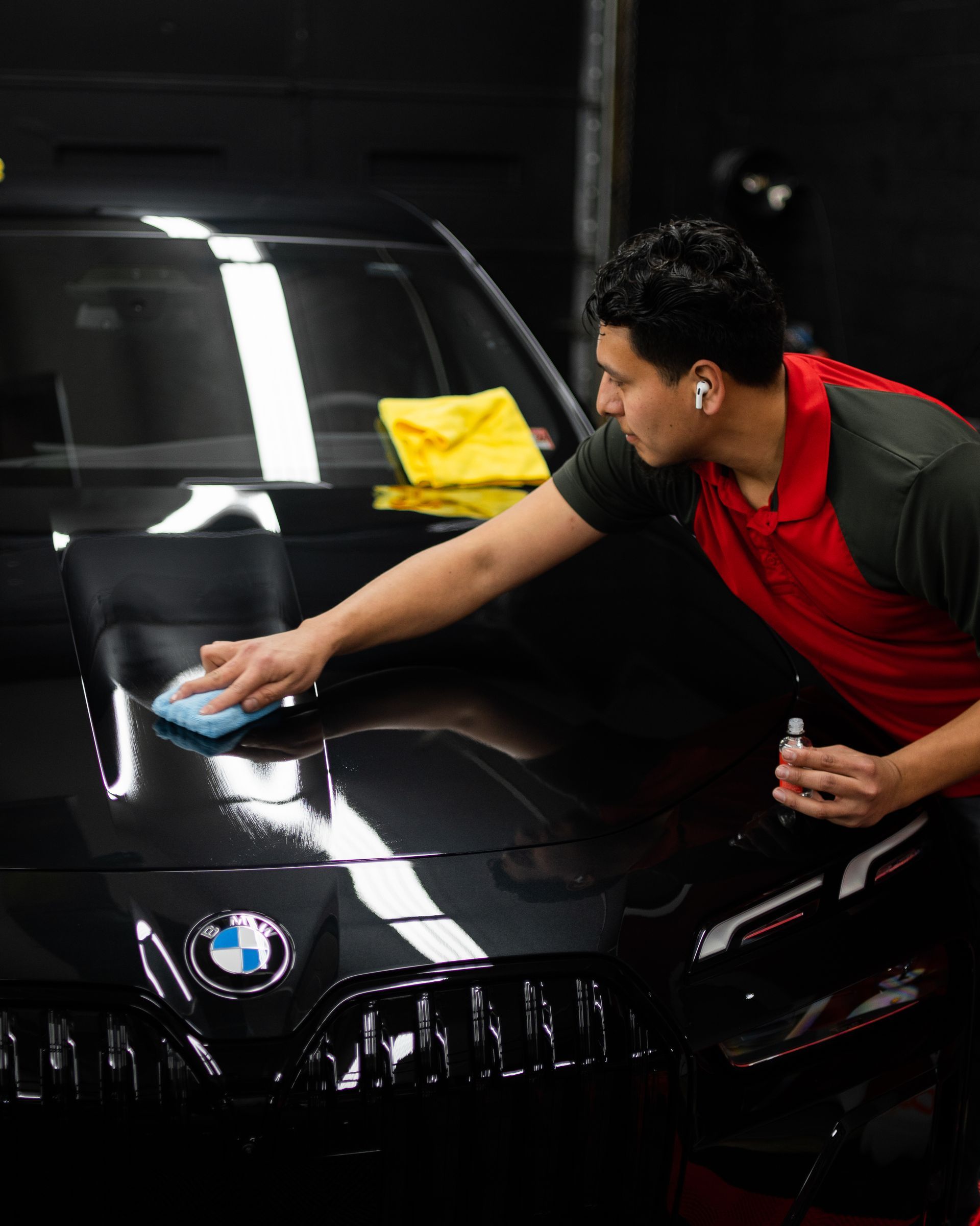 A man is cleaning the hood of a black bmw with a cloth.