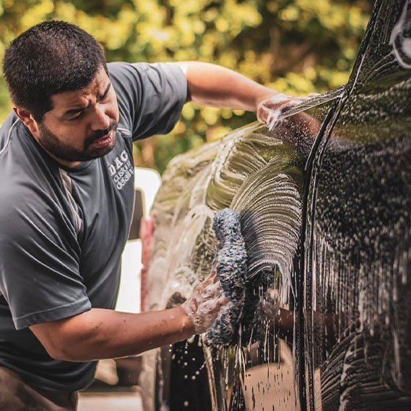 A man in a grey shirt is washing a black car