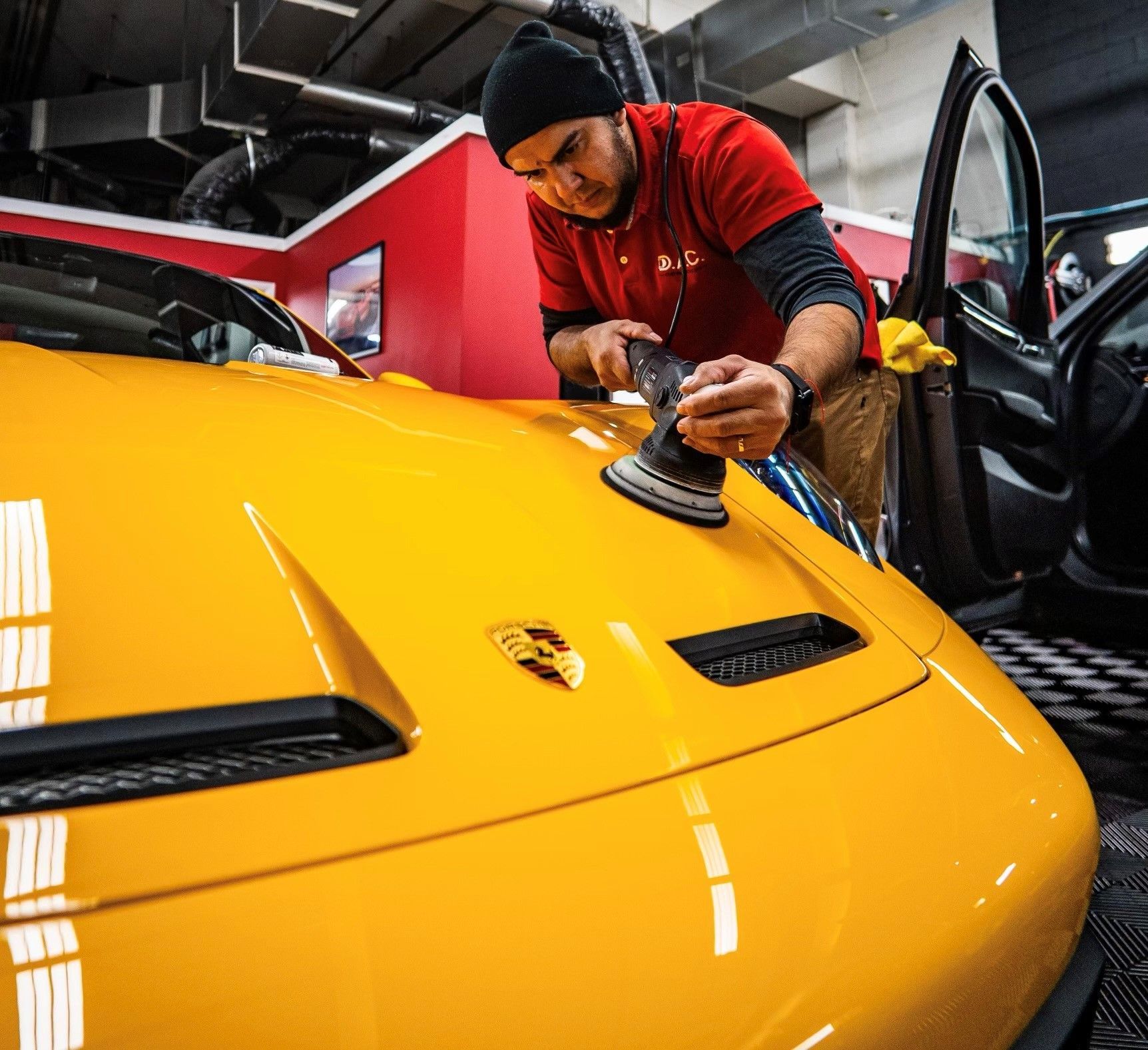 A man in a red shirt is polishing a yellow sports car