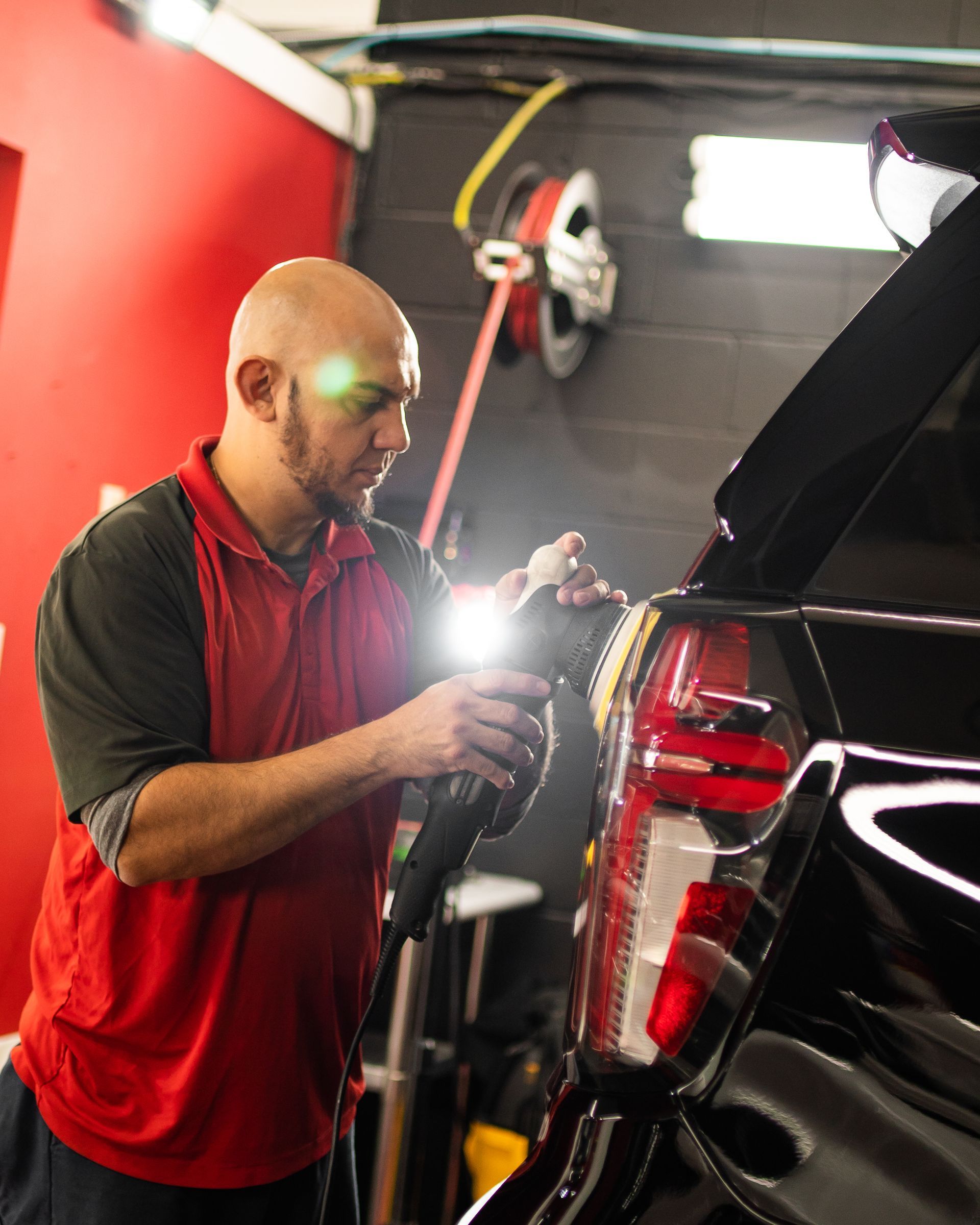 A man in a red shirt is polishing a black car