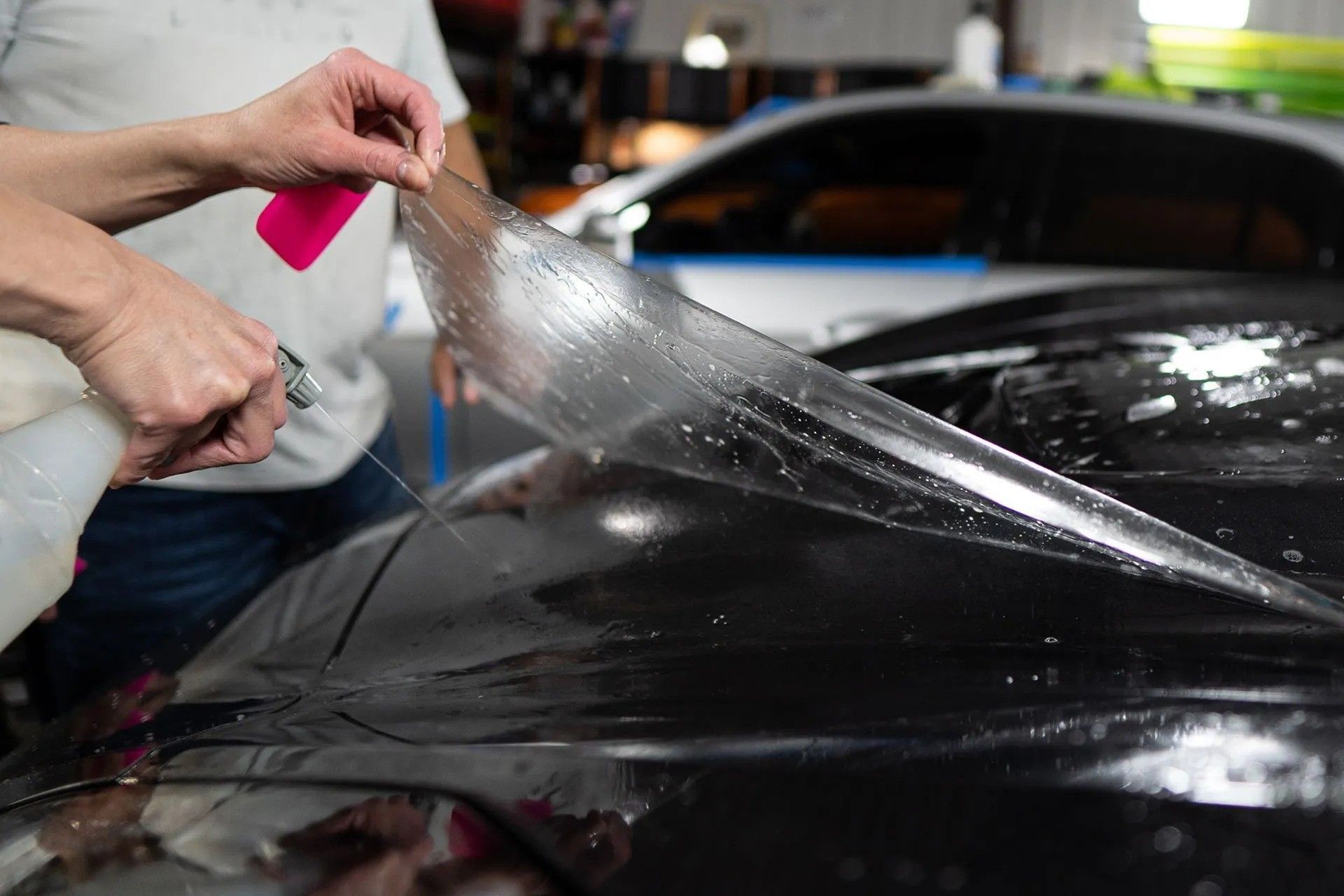 A person is applying a protective film to the hood of a car.