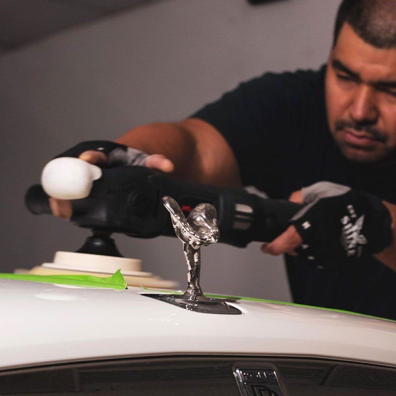 A man is polishing the hood of a white car